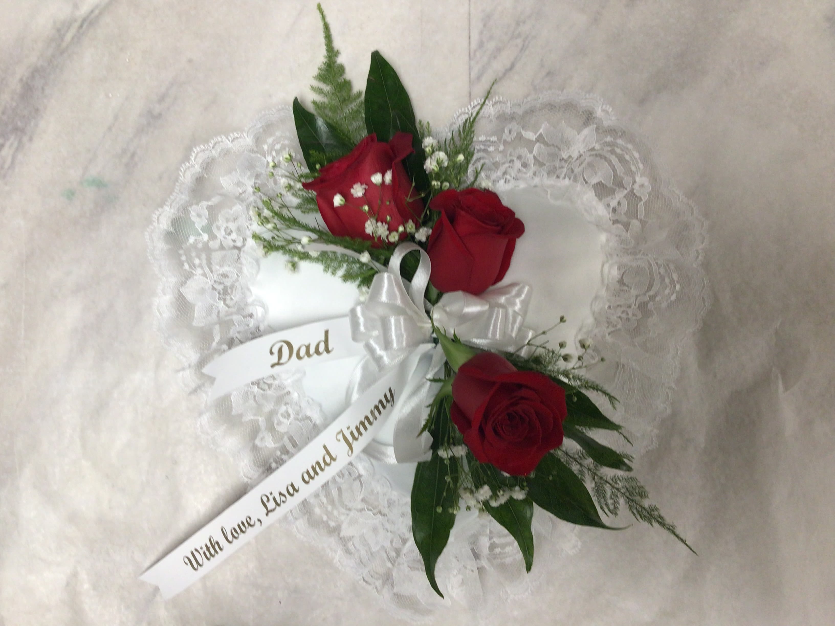 Satin Casket Heart Satin Casket Heart - A small satin heart pillow adorned with 3 red roses, babies breath, and greens. This is a sentimental tribute that is usually placed in the lid of the casket.
