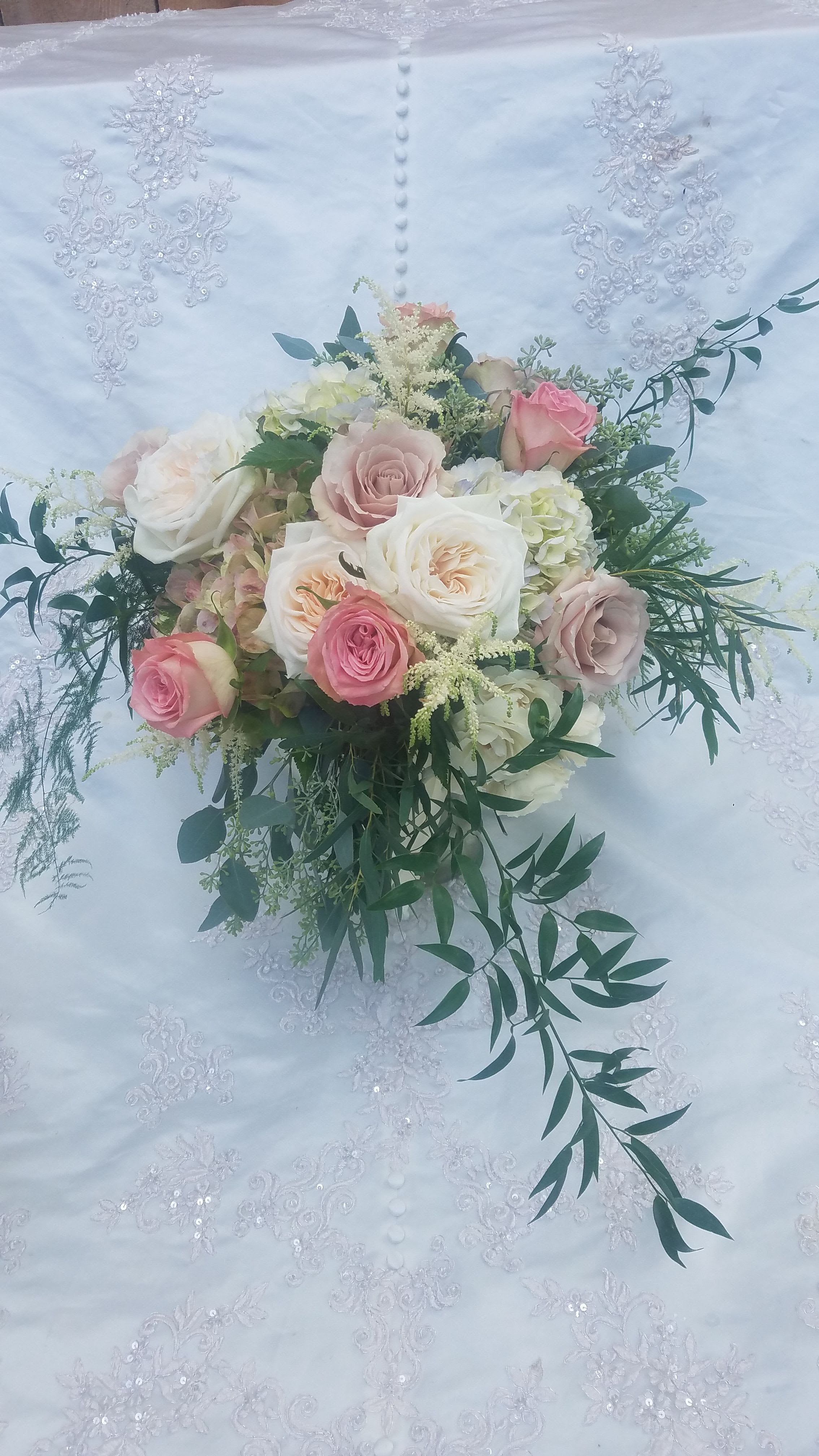 Bride's Bouquet - Soft Elegant Blush - The palette of white, ivory, and blush blooms creates a timeless and romantic feel, perfect for a wedding day. Classic traditional roses form a base of subtle structure, while the ruffled charm of garden roses adds a touch of luxurious softness. Delicate spray roses punctuate the arrangement with tiny bursts of color, harmonizing with the bell-shaped lisianthus, which dance among the other florals. Wispy astilbe adds a feathery texture and movement, complementing the silvery-green tones of assorted eucalyptus which provides a sophisticated backdrop. This popular wedding color theme allows the subtle variations in tone to create depth and visual interest, ensuring that the bouquet becomes a cherished focal point, adding a touch of refined beauty to your special day. All our floral creations are lovingly handmade in our shop, ensuring each piece receives the attention and care it deserves. To guarantee the freshness of your wedding flowers, we require all wedding packages to be ordered at least 3 weeks in advance and are available for pick up only in our shop, ideally on the morning of your wedding.  Should your needs extend beyond the bouquet, additional items may be purchased from our a la carte selection, allowing you to fully customize your wedding floral arrangements.
