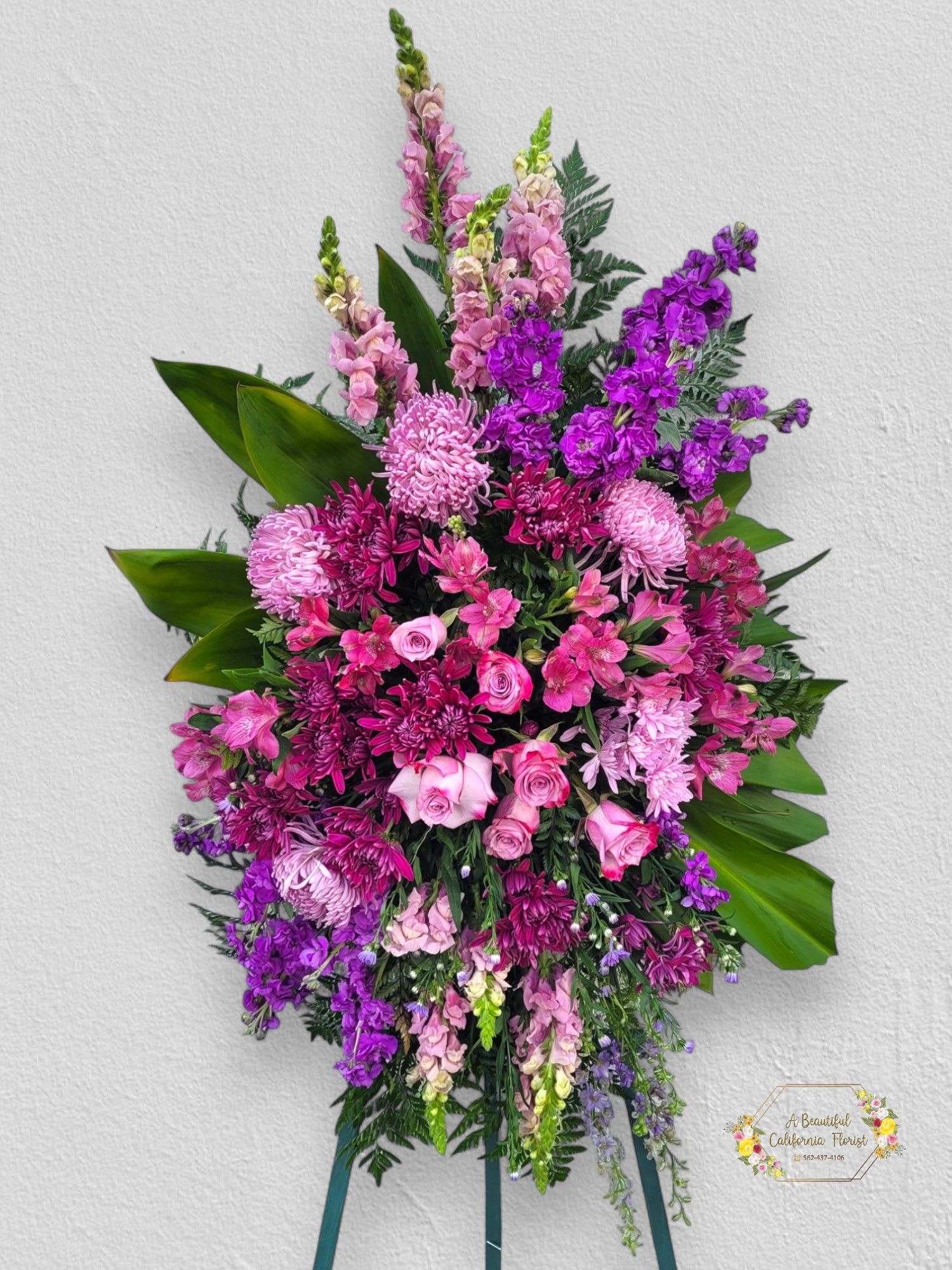 Lavender Grace Standing Spray Lavender Grace Standing Spray - Lavender Grace Standing Spray, A graceful and elegant standing spray in soothing shades of lavender, pink and purple. Delicate roses, snapdragons, stock and chrysanthemums are artfully arranged with lush greens of ti leaves and palm. This exquisite display, standing tall on a 5.5 ft wood easel, offers a serene tribute to a beloved soul.