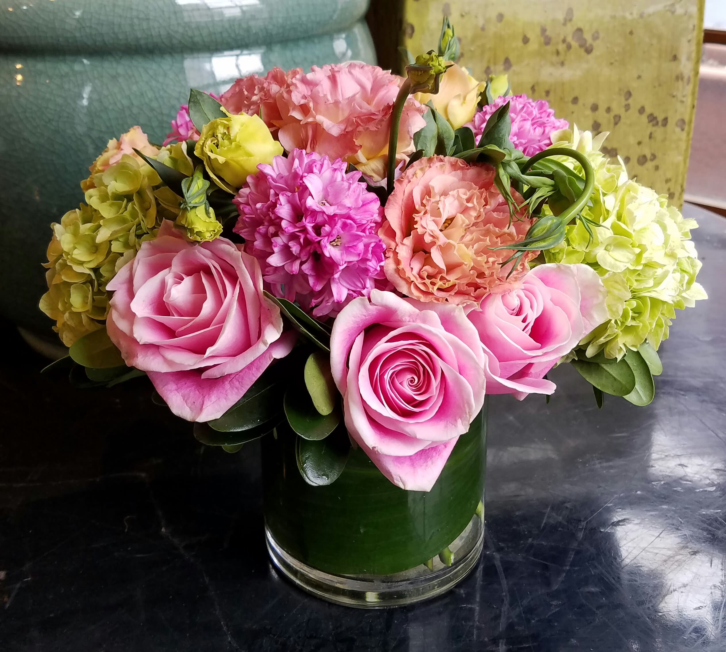 Dora's Adventure - The fun and lively arrangement features beautiful pink Roses, fragrant Hyacinth, lush, green Hydrangea along with a variety of complementary blooms in a leaf wrapped glass cylinder.