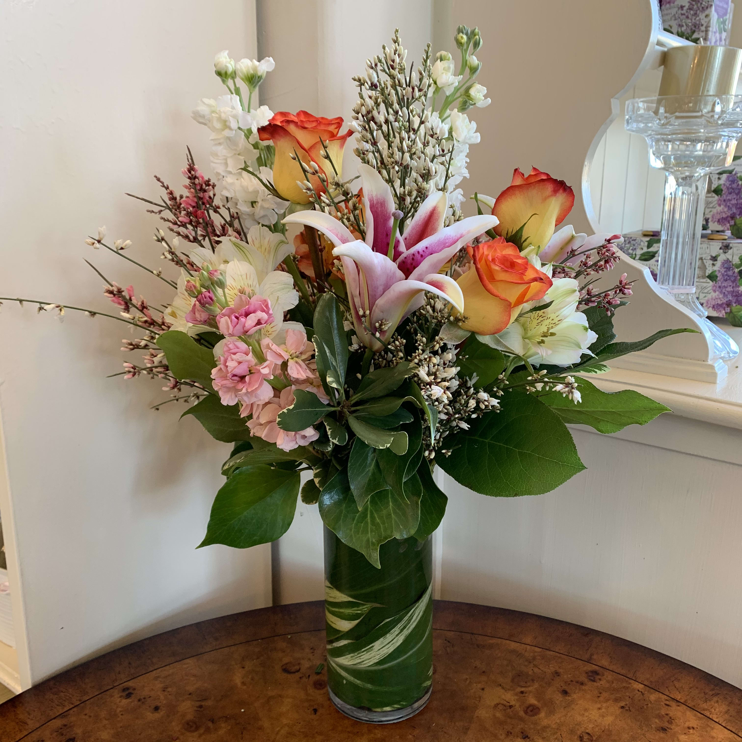 Hello Doll - Circus roses, stargazer lily, white and peach stock, and white alstromaria arranged in a leaflined 7in cylinder with white and pink ginestra. Approximatly 15in tall and 10in wide. 