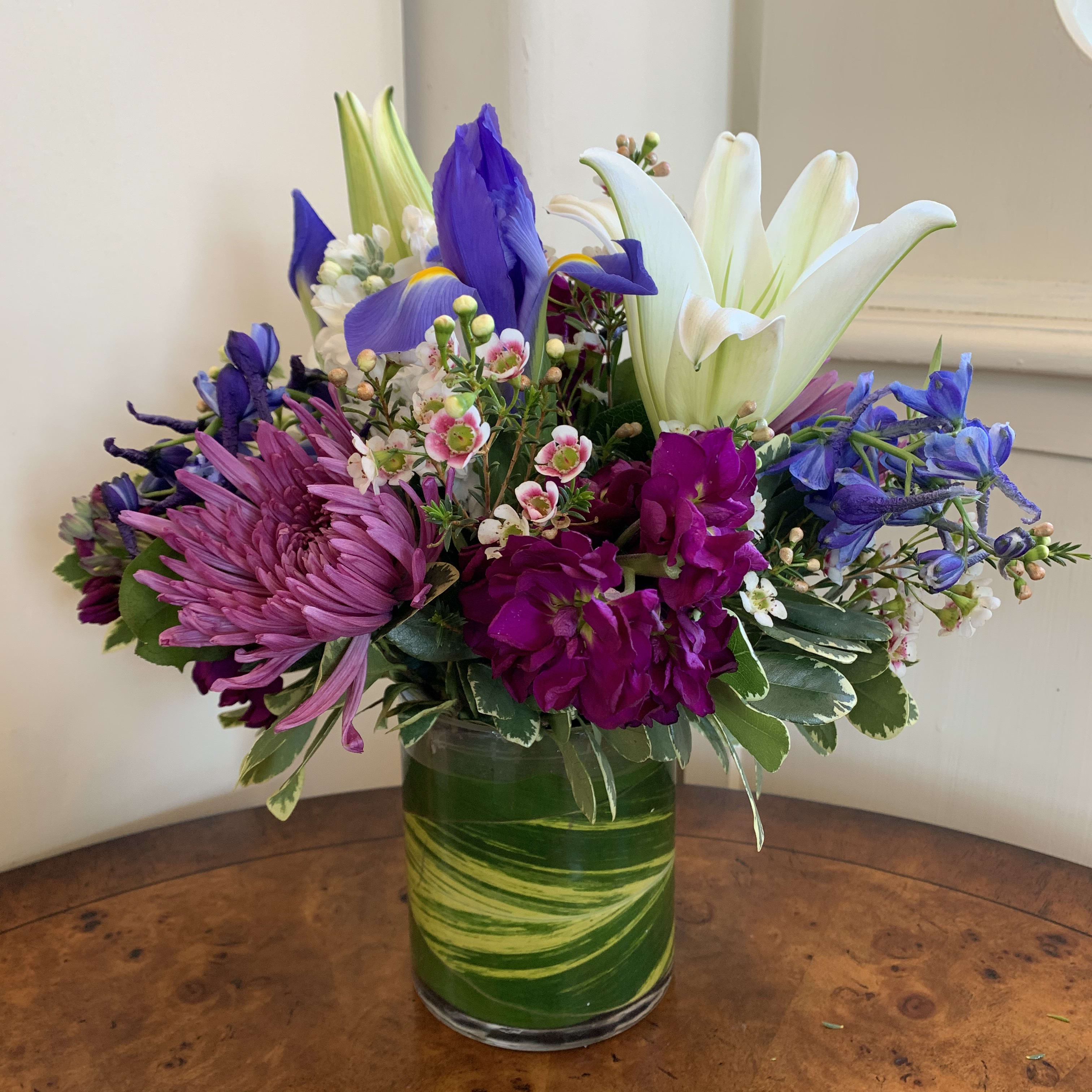 Moonstruck  - White lily, iris, white and purple stock, blue delphinium, lavender spidermums arranged in a small leaflined gather with white waxflower. Approximatly 10in tall and 8in wide. 
