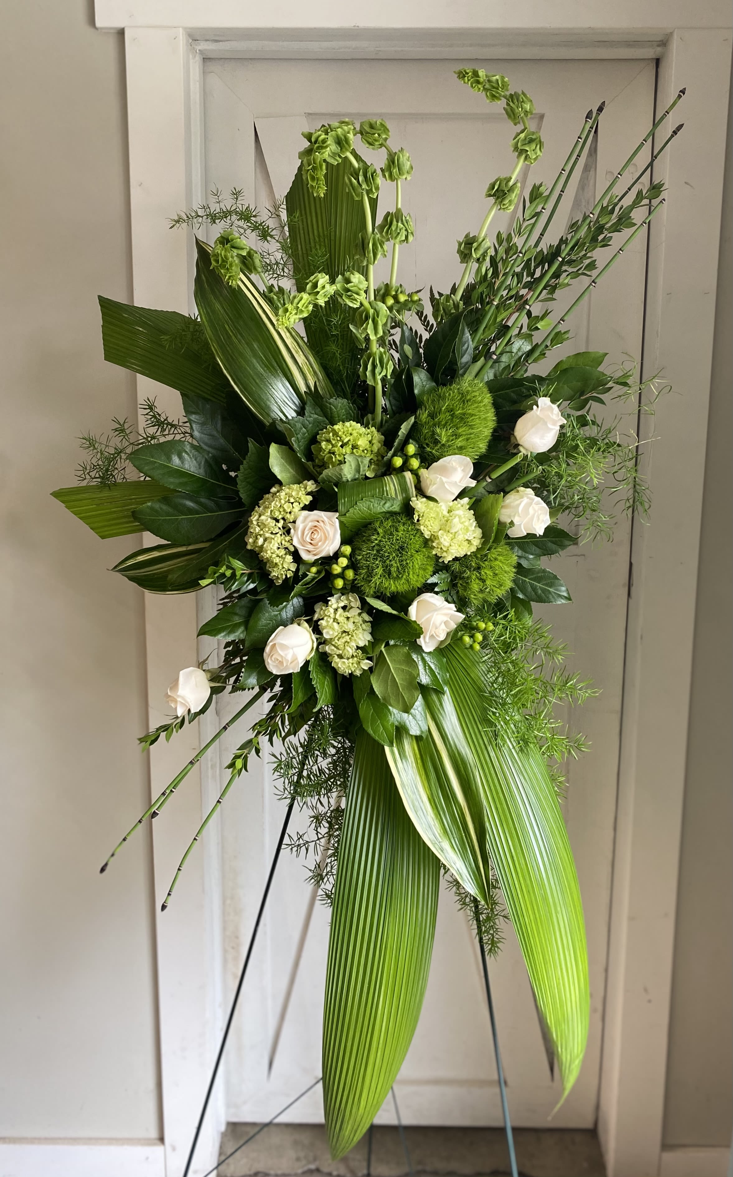 Forever At Peace Forever At Peace - A peaceful display of affection and sympathy this monochromatic spray of gorgeous fresh greens and pure white roses is a vision of tranquility. This tranquil spray of miniature green hydrangea green roses green trick dianthus and bells of Ireland is accented with bupleurum myrtle sword fern variegated aspidistra leaves aralia leaf bear grass and lemon leaf. Delivered with a wire easel.