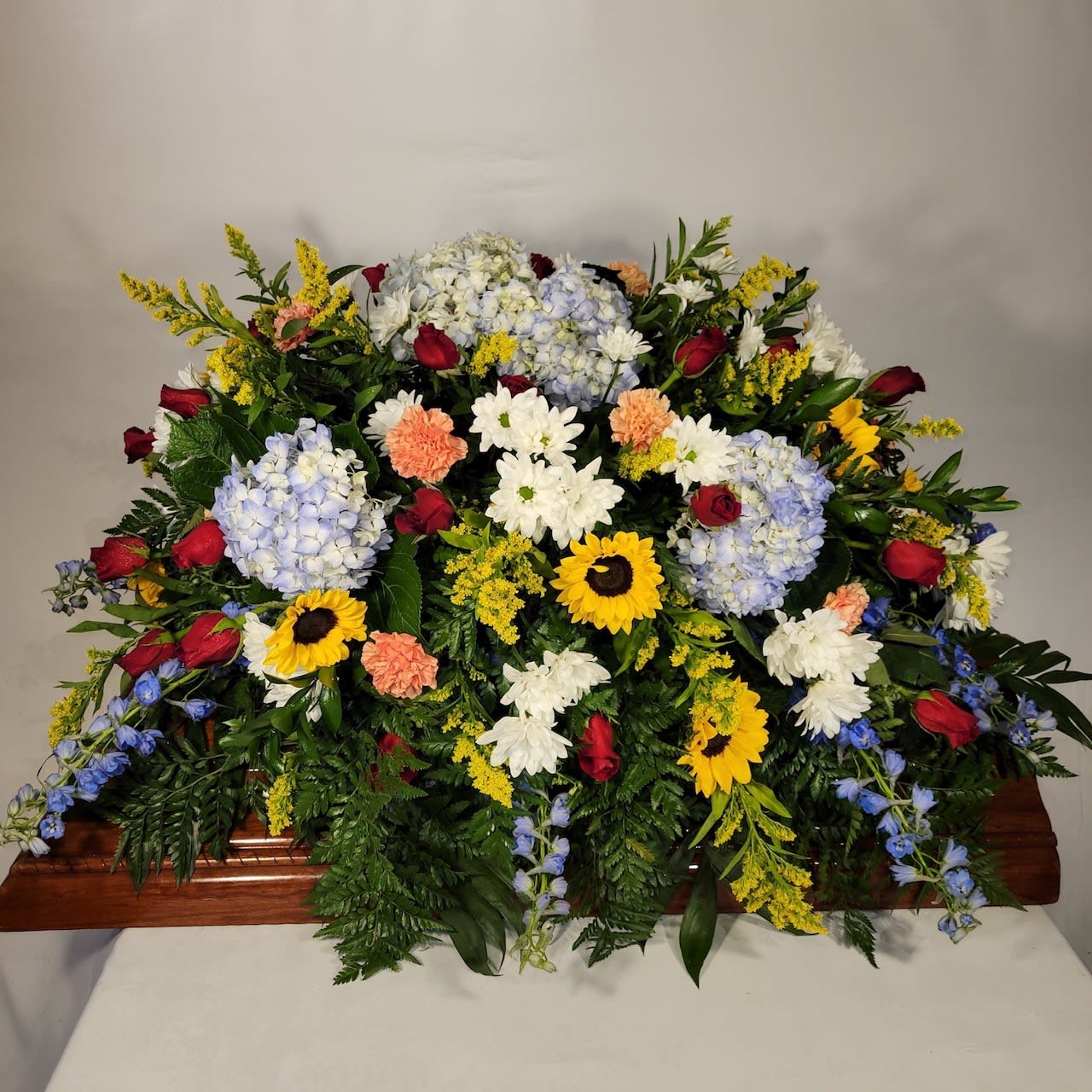 Sunflower & Rose Casket Spray Sunflower & Rose Casket Spray - This casket spray has Red Roses, Sunflowers, Blue Hydrangeas, White Daisies, Orange Carnations, Blue Delphinium and Solidago.