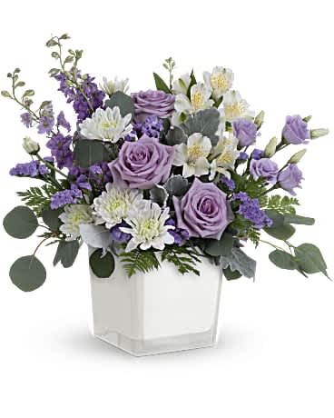 Teleflora's Honey Lavender Blooms Bouquet - Loveliest lavender! Make any day feel extra special with the soft purple hues of this luxurious rose bouquet, presented in a soft white glass cube. Lavender roses, white alstroemeria, lavender lisianthus, lavender larkspur, white cushion spray chrysanthemums and lavender sinuata statice are arranged with dusty miller, leatherleaf fern and silver dollar eucalyptus. Delivered in Teleflora's Color Splash cube. Orientation: All-Around  SUBSTITUTION POLICY – Always deliver the freshest flowers! Please note the bouquet pictured reflects our original design.  If the exact flowers or container in this arrangement are not available, our local florists will create a beautiful bouquet with the freshest available flowers.