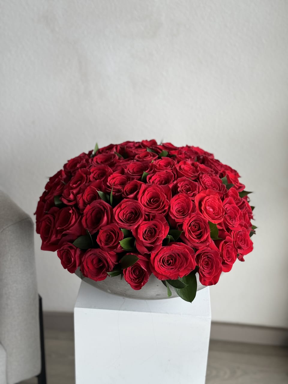 75 Red Roses in a Concreate Vase - 75 red roses arranged in a chic concrete vase, a striking fusion of passion and modern elegance. The deep crimson blooms exude love, while the industrial charm of the vase adds a touch of contemporary sophistication. An opulent centerpiece that captivates with its abundance and style.