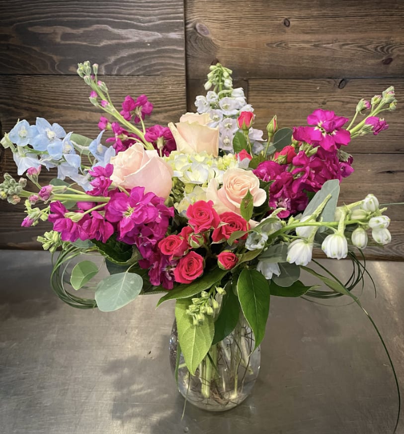Stepping into Spring  Stepping into Spring  - A full arrangement of pleasantly pastel colors and flowers, including blue hydrangea, blue delphinium, light pink roses, magenta stock, pink spray roses and a mix of greenery.  Approx. 20" T x 17" W