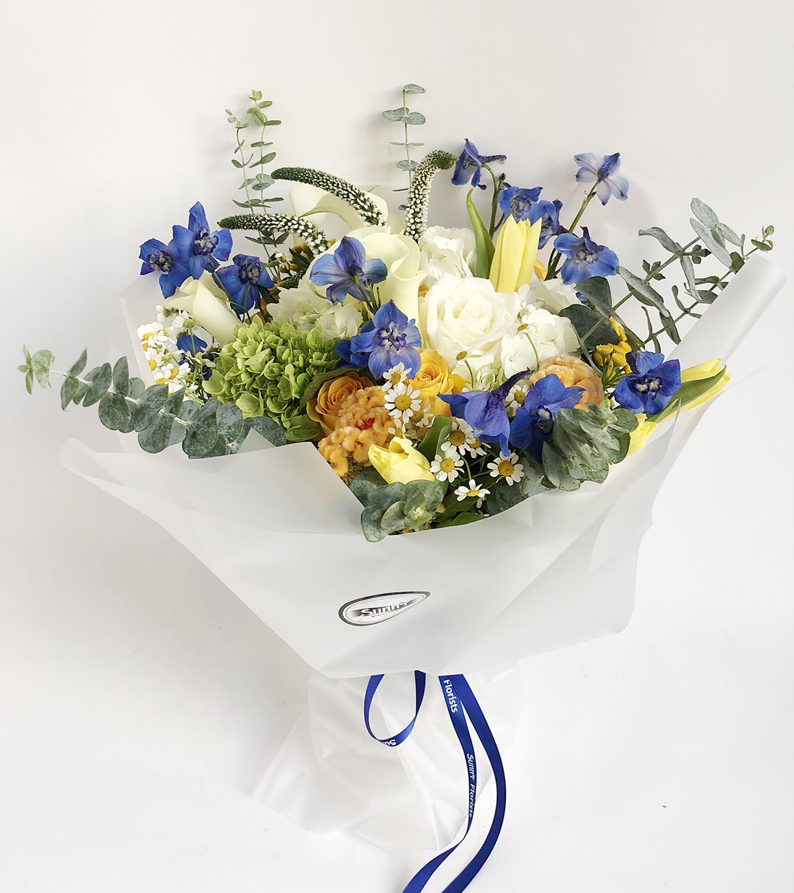 Southie - Named after our shop’s neighborhood, our beloved Southie is fun and one-of-a-kind! This handtied bouquet features a variety of white, blue, and yellow flowers, accented with green hydrangea and eucalyptus. Flowers may include cockscomb, Flowers and vase will vary based on availability.