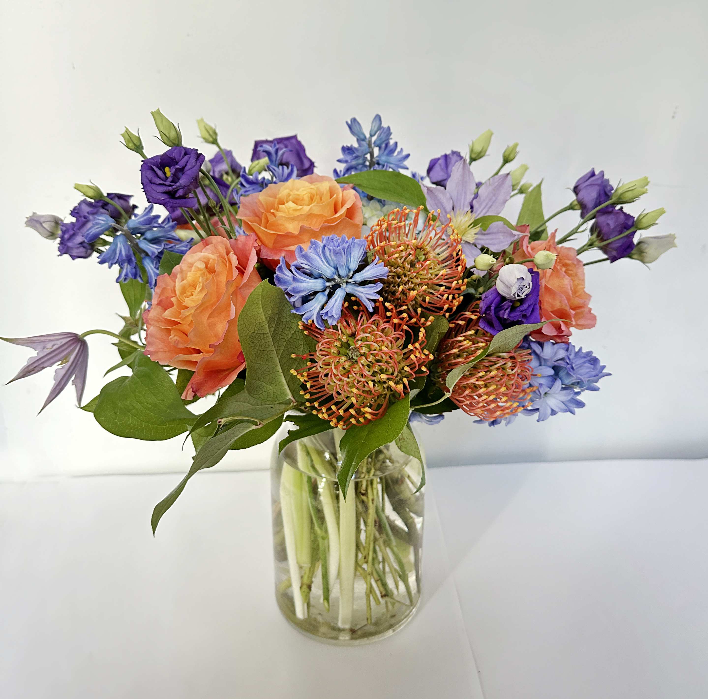 Summer Splender Summer Splender - This arrangement is presented in a milk jar glass. It features bright orange and purple spring color. The arrangement includes hydrangeas, orange free spirit roses, orange pincushions, purple/blue hyacinth, lavender clematis, purple lisianthus with assorted greens.