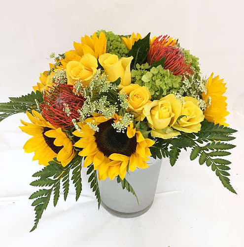 Sunny Day Sunny Day - This arrangement uses yellow, green and orange to bright somebody's day.   Size: about 11"*12" Flowers: Sunflowers, Yellow Roses, Queen Anne's Lace, Pincushion, Mini Green Hydrangea, Feather Leaves.