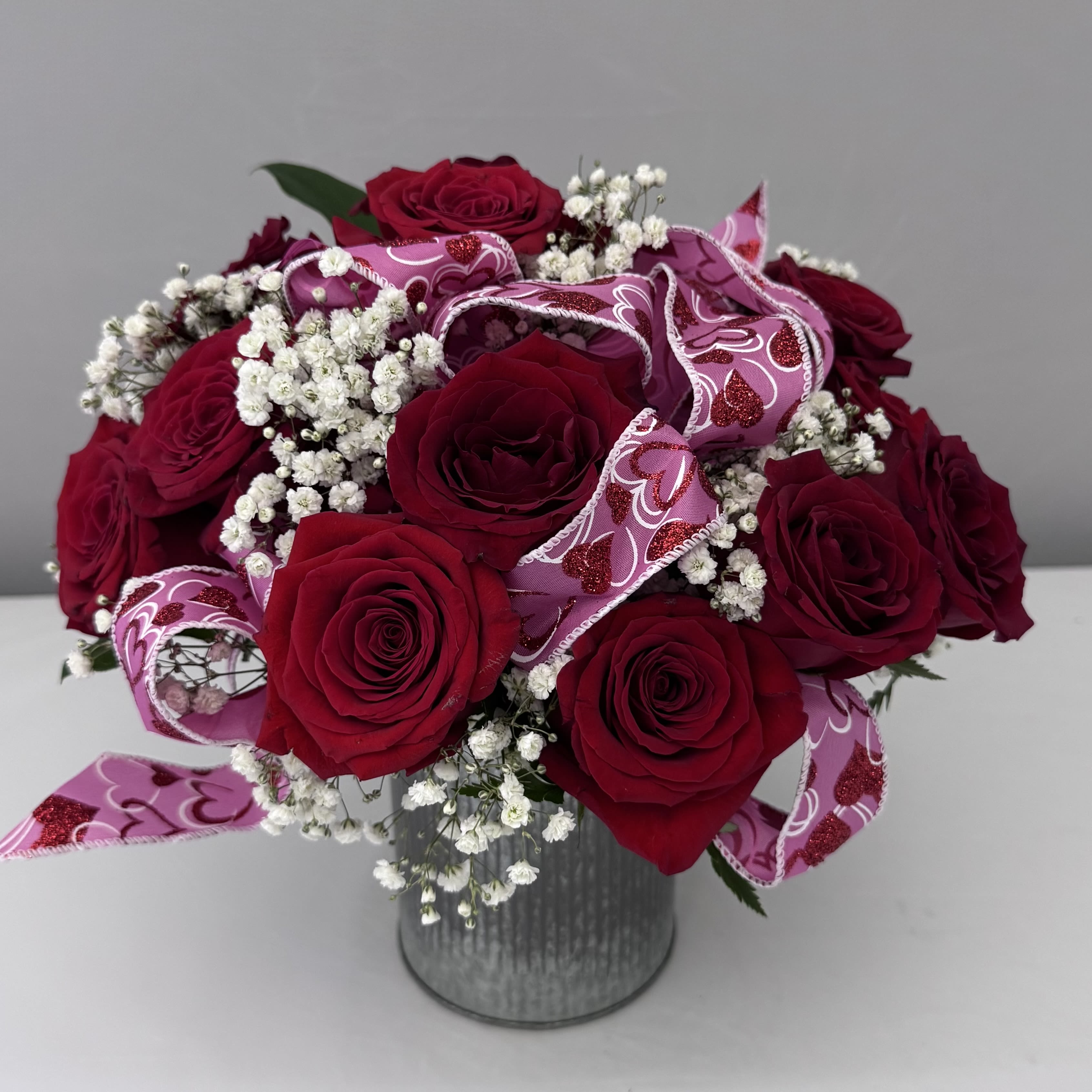 LOVER'S EMBRACE  - DOZEN RED ROSES ACCENTED WITH A HEART BOW AND BABY'S BREATH IN A 5X5 METAL CORRUGATED TIN.  
