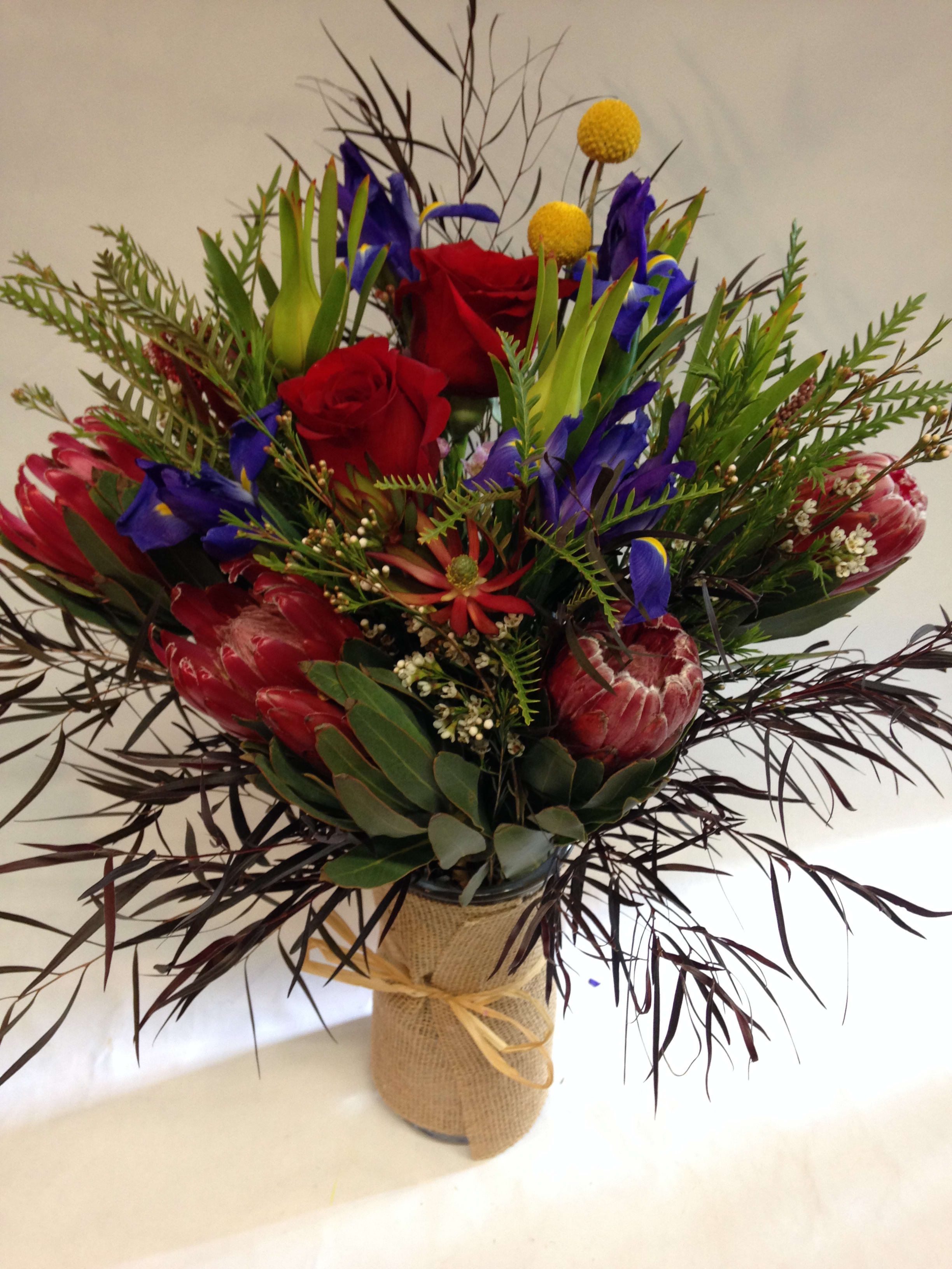 Protea Elegance.  ( LONG LASTING) - This long lasting arrangement is comprised of proteas, irises, red roses, safari branches, billy balls and various greenery.  (Some flowers may be subject to change depending on the season. We will contact you with available flower substitutions; please contact us with specific questions if you are concerned with flower availability, thanks!)  Featured arrangement: $145.00 (Regular Price)