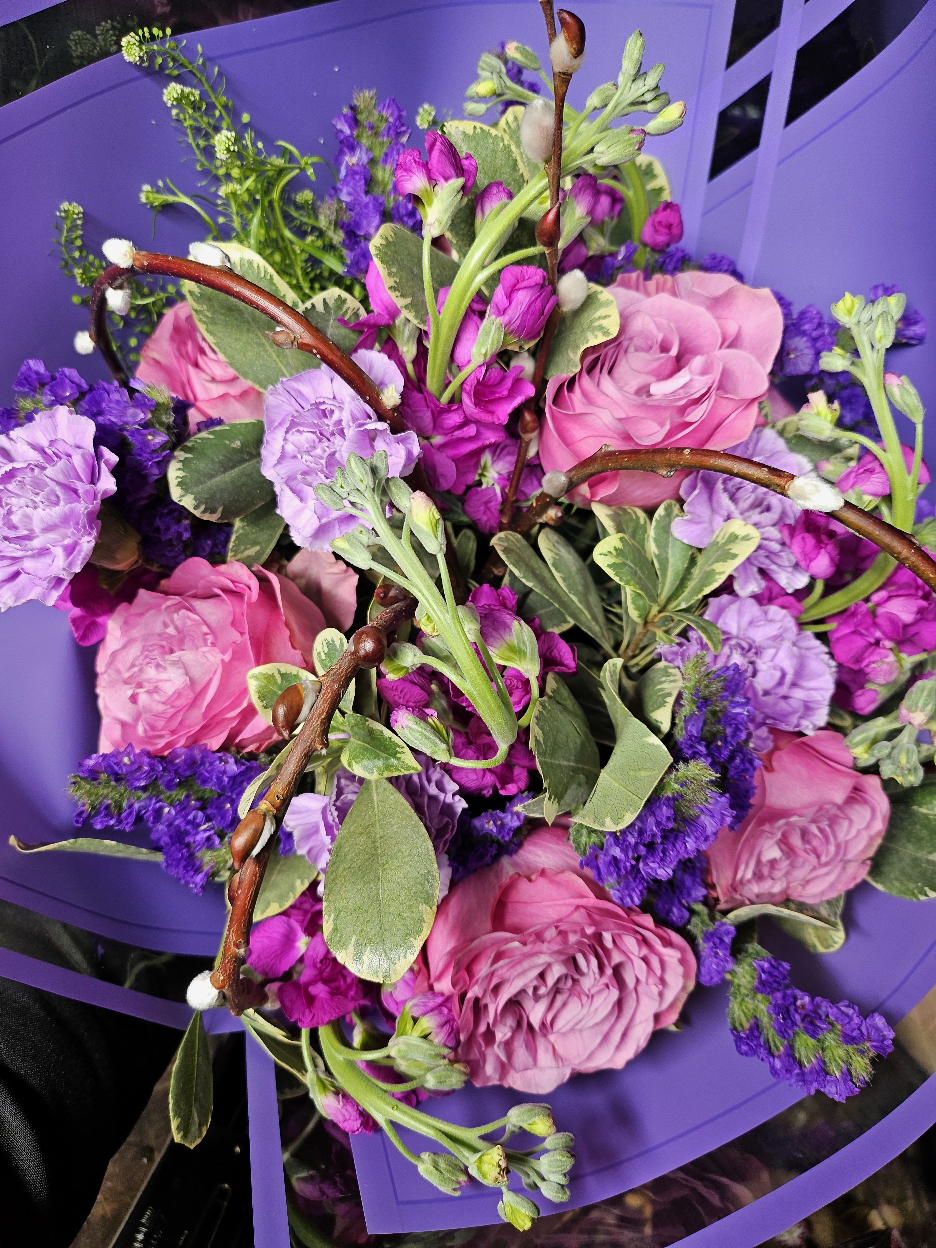 Radiant Lavender Bliss Bouquet - Indulge in the mesmerizing hues of this &quot;Radiant Lavender Bliss&quot; bouquet. Featuring a luxurious blend of lavender carnations, soft pink roses, delicate spray roses, and accent blooms in varying shades of purple. Enhanced with lush greenery and charming details like pussy willow branches, this arrangement radiates elegance and charm. Perfect for any occasion, from heartfelt anniversaries to uplifting moments of appreciation. Delivered wrapped in premium violet wrapping, it’s ready to bring joy to any room.