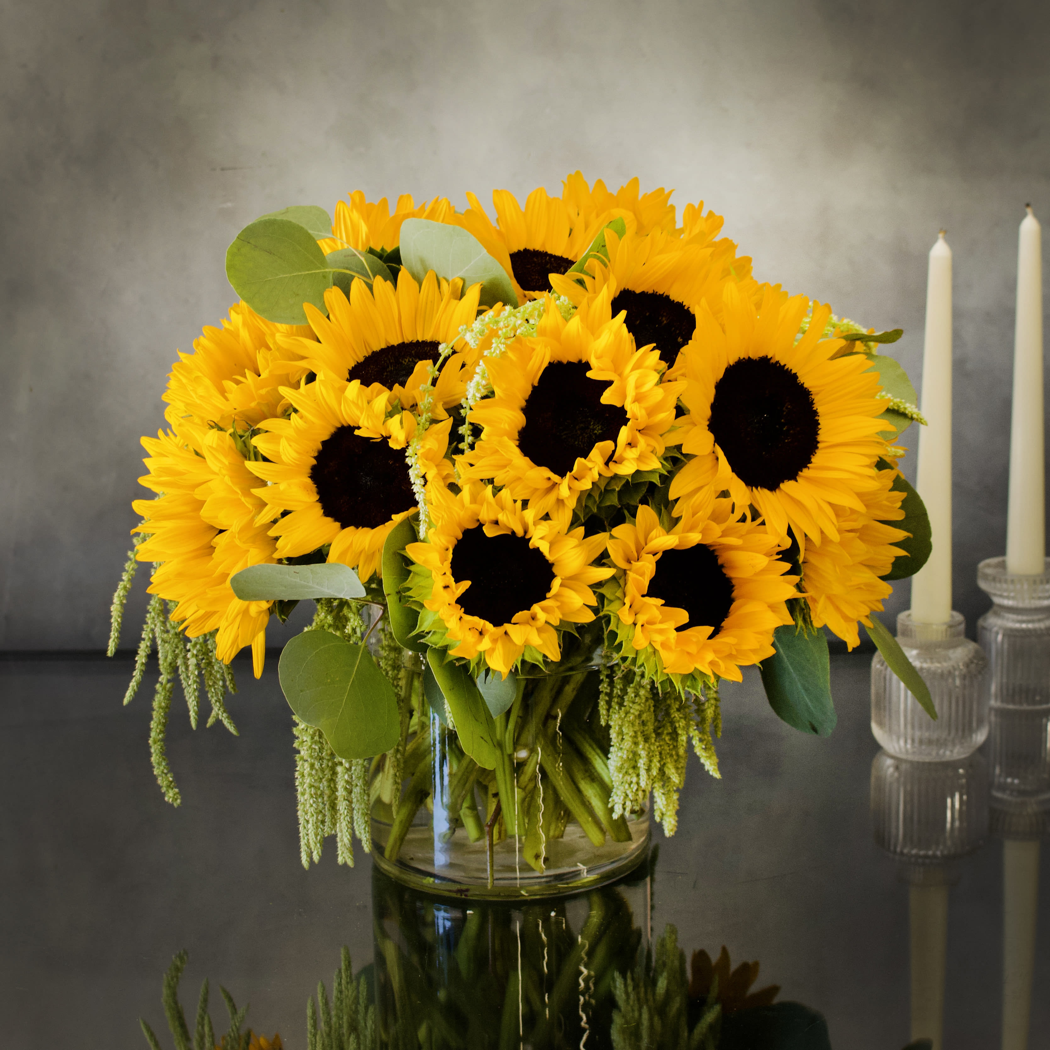 Here Comes The Sun - Pasadena Florist - A bright arrangement of Sunflowers ! A classic with a beautiful green touch with our seasonal greens. Adding a chic touch to a sunny arrangement. Placed in a clear glass Cylinder 6x6 vase. 