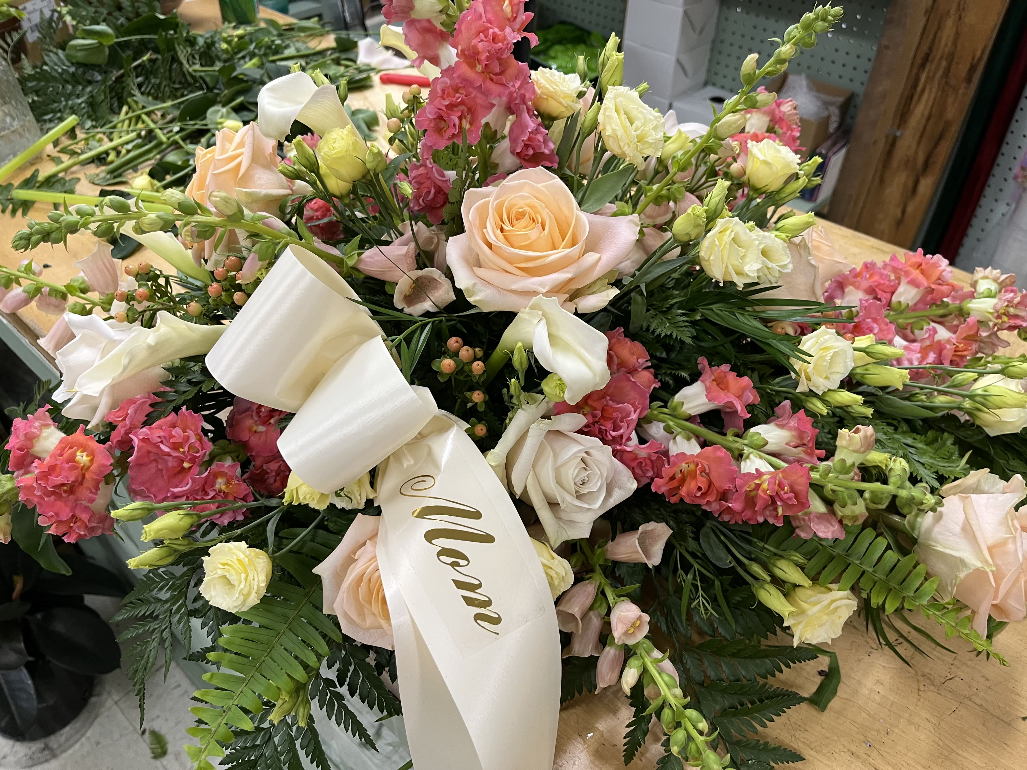 Small custom casket spray - This small casket spray is made with roses, foxglove, spray roses, and mixed greens accompanied by a customizable ribbon. 