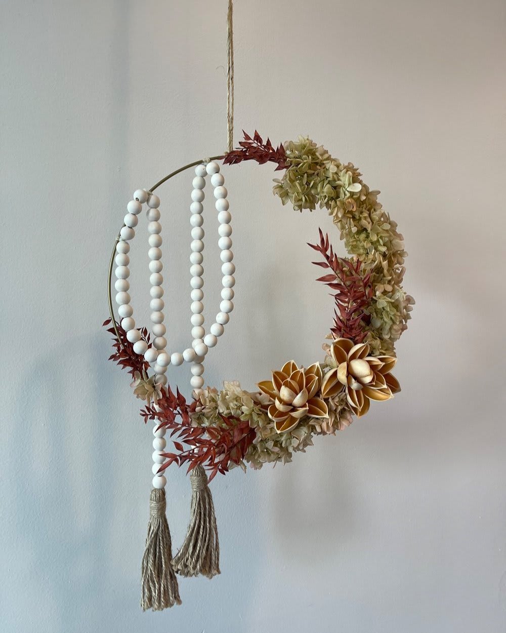 BLOOMING - - Hanging floral arrangement with circular design - Pale red blooms and verdant green foliage - Flowers protruding gracefully on one side - Asymmetrical composition for visual dynamism - Blends natural elegance with artistic flair   