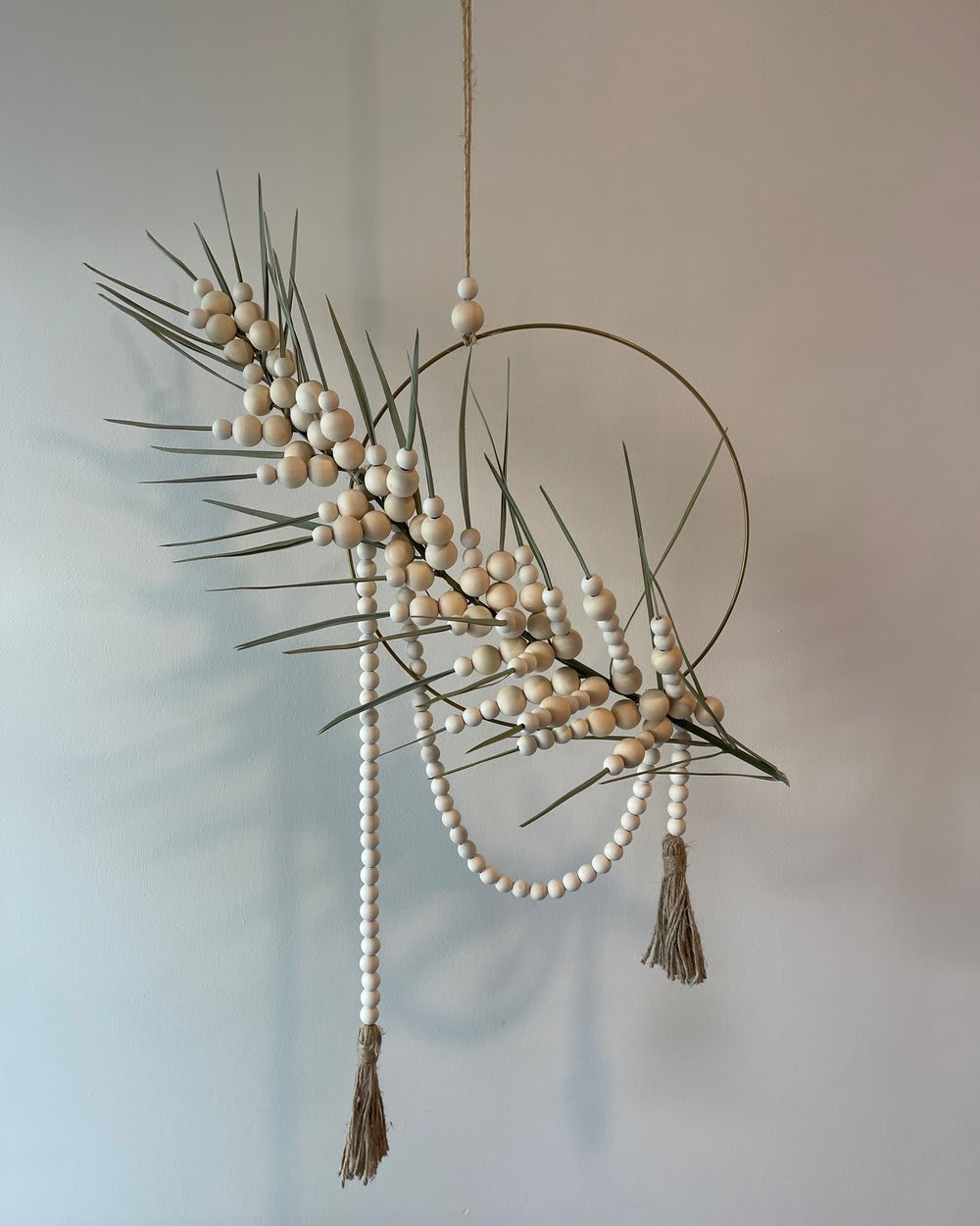 CONNECTED - - Circular hanging floral arrangement with graceful palm frond - Intertwined with delicate beaded accents - Harmonious blend of nature and artistry - Brings tropical tranquility and bohemian elegance - Invites admiration of serene beauty from every angle