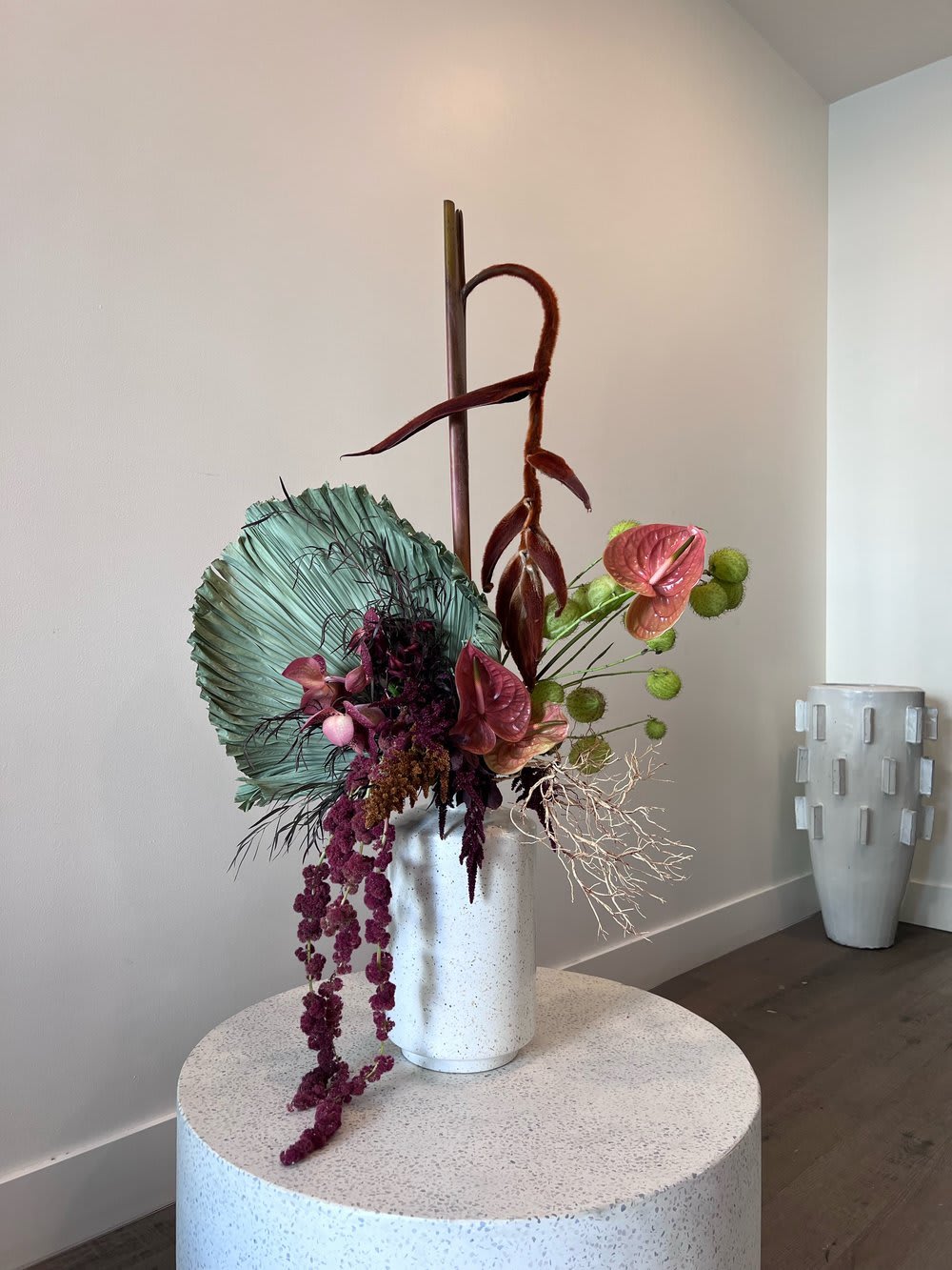 SEASONS - ORBIT - - Vase floral arrangement exuding dramatic allure - Tall, dark plants standing prominently - Deep red and green floral accents - Subtle dried plants add texture - Rich color palette and contrasting elements - Creates sophisticated and captivating centerpiece