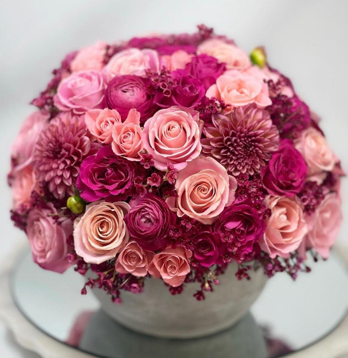 Violet Kingdom Violet Kingdom - Sumérgete en el mágico reino de las violetas con este arreglo floral que te transportará a un mundo de romance y elegancia. Las rosas y otras flores en tonos violetas, fucsias, morados y rosados se unen para crear un efecto visual impresionante, lleno de color y textura.