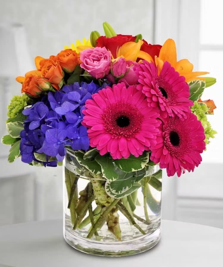 Brightness - A small cubed centerpiece with blue hydraganea, pink gerbera daisies, orange and pink spray roses