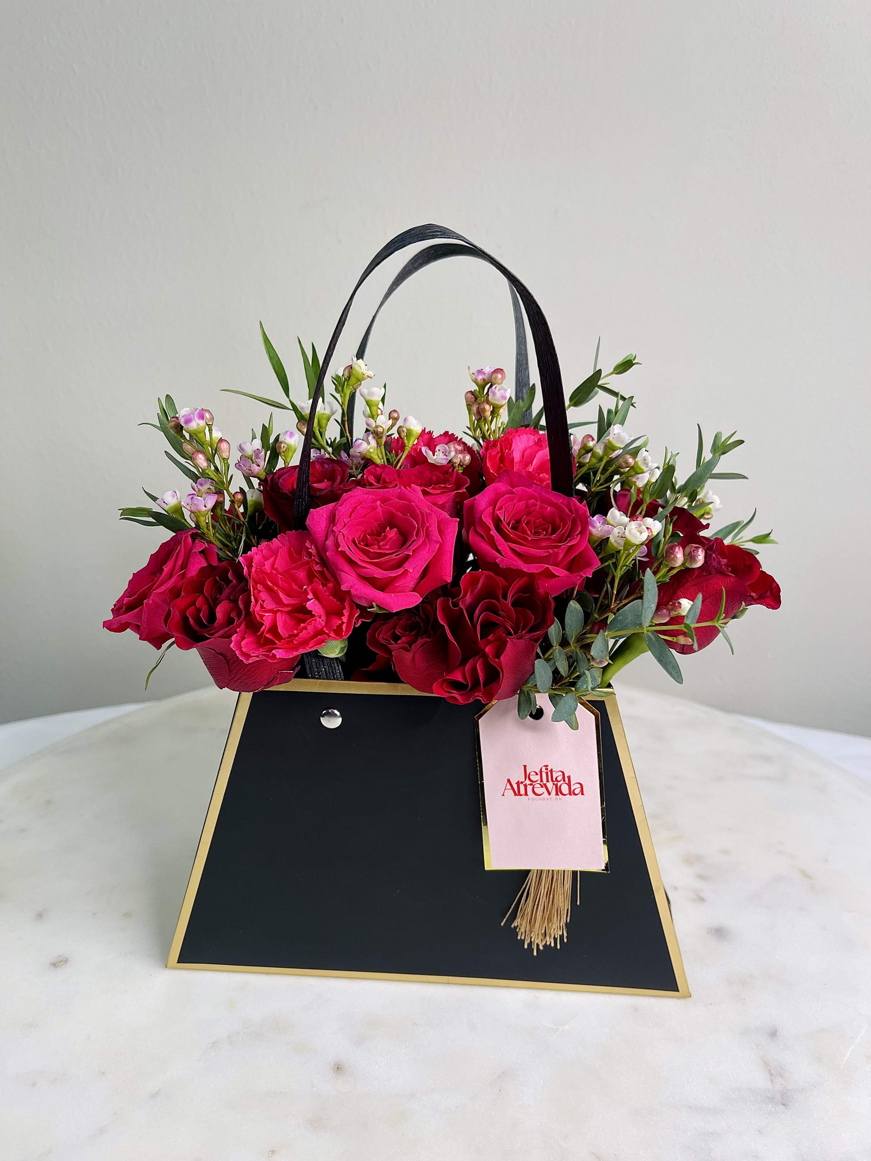 The Jefita Atrevida Goddess Bag - Celebrate Love with Purpose This Valentine’s Day!  Introducing the Jefita Atrevida Goddess Bag - a stunning floral arrangement that embodies elegance, love, and empowerment. This exquisite bag is not just a beautiful gift; it’s a statement piece that supports a noble cause.   Crafted with lush, vibrant red roses and delicate pink blooms, the Goddess Bag is designed to capture hearts and elevate any occasion. Its chic, modern silhouette features a sleek black exterior, perfectly accentuated by a stylish handle and an elegant tag showcasing the Jefita Atrevida logo.   Why Choose the Goddess Bag? - Empowerment with Every Purchase: For every bag sold, Mas Flora proudly donates $5 to the Jefita Atrevida Foundation. Your purchase helps empower women and first-generation students, providing them with essential resources, mentorship, and community support. - Sustainable &amp; Stylish: This eco-friendly arrangement is designed to last, making it a sustainable choice for your floral needs.  Show your love this Valentine’s Day with the Jefita Atrevida Goddess Bag. Experience the joy of gifting while contributing to a greater cause. Order now and be part of the ripple effect of change—one gorgeous floral arrangement at a time!  Customization: Please leave your preferred initial letter in the special instruction box at check out for each bag ordered and we will create a custom tag for each bag! 