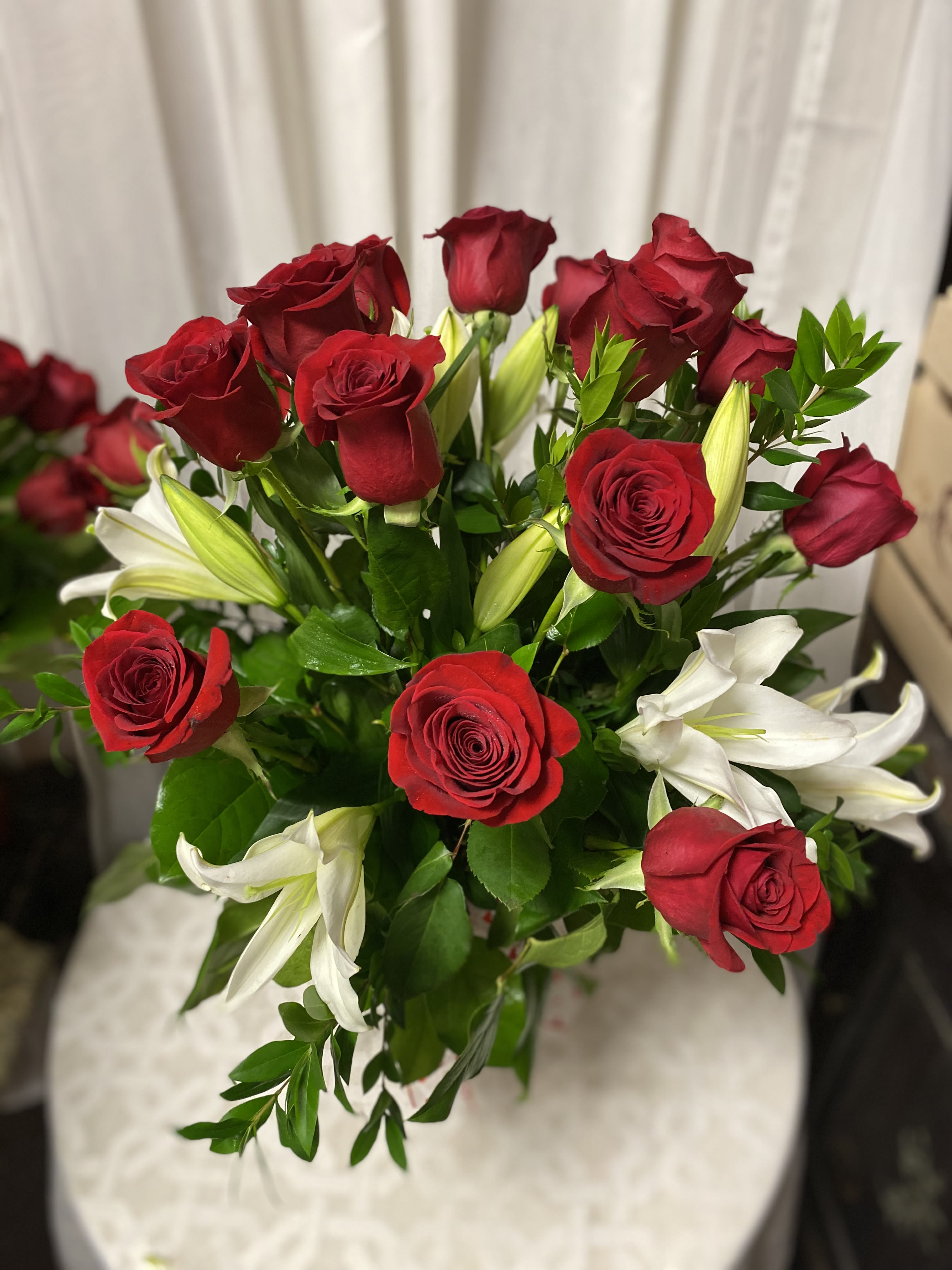 Endless Devotion - The Endless Devotion arrangement is a captivating blend of bold red roses and graceful white lilies, symbolizing passionate love and pure intentions. The vibrant red roses represent deep affection, while the elegant lilies add a touch of serenity and sophistication. Accented with fresh greenery and arranged in a red glass vase, this bouquet is the perfect statement of enduring love and admiration.