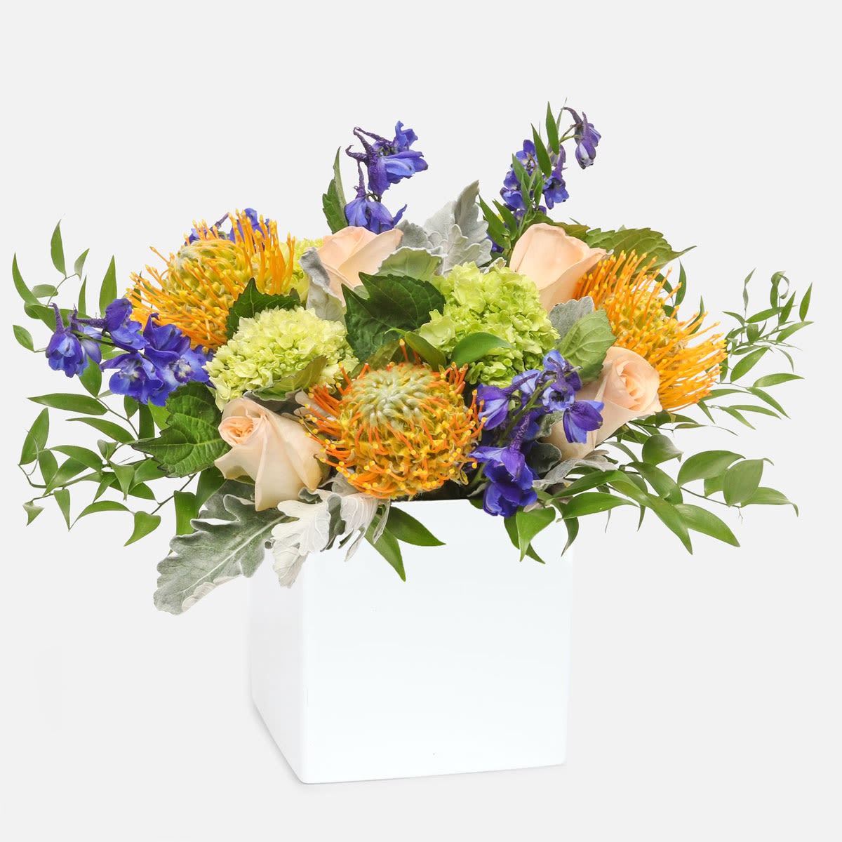 Montauk - [ Height: 12'' - 13'' | Diameter: 15'' - 16'' ]  A colorful arrangement that embodies the laid-back cool of Montauk. Orange pincushion protea, blue delphinium, peach roses and mini green hydrangea blooms in a geometric ceramic container that they’ll surely want to use again and again.   PlantShed hand-delivers flowers and plants to any borough of NYC, 7 days a week. 