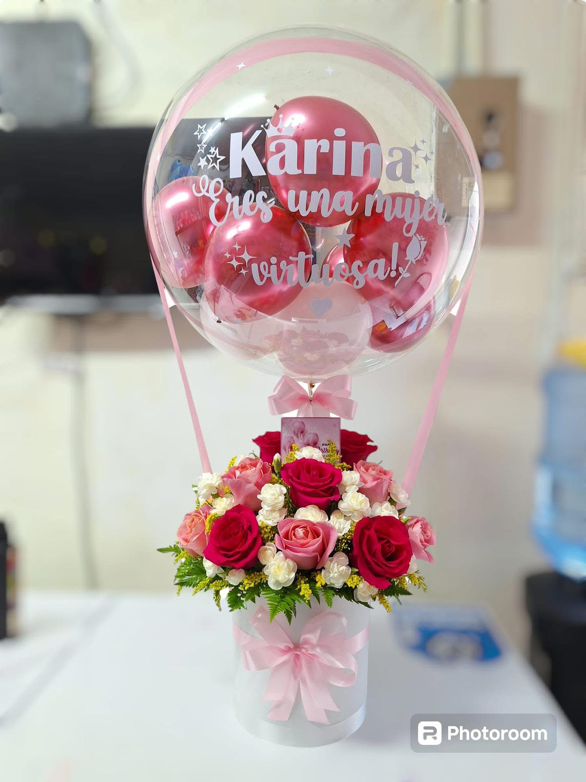 karina's birthday - Este arreglo floral combina elegancia y romanticismo. Está compuesto principalmente por rosas rojas y blancas, colocadas en un diseño simétrico y bien equilibrado. Las rosas rojas, símbolo de amor y pasión, están rodeadas de las blancas, que transmiten pureza y armonía. La base incluye hojas verdes que aportan frescura al diseño.  En la parte superior del ramo, hay un globo transparente decorativo que parece tener un mensaje personalizado, visible en letras blancas, añadiendo un toque especial y personalizado al conjunto. Es un arreglo ideal para celebraciones románticas o conmemoraciones especiales.