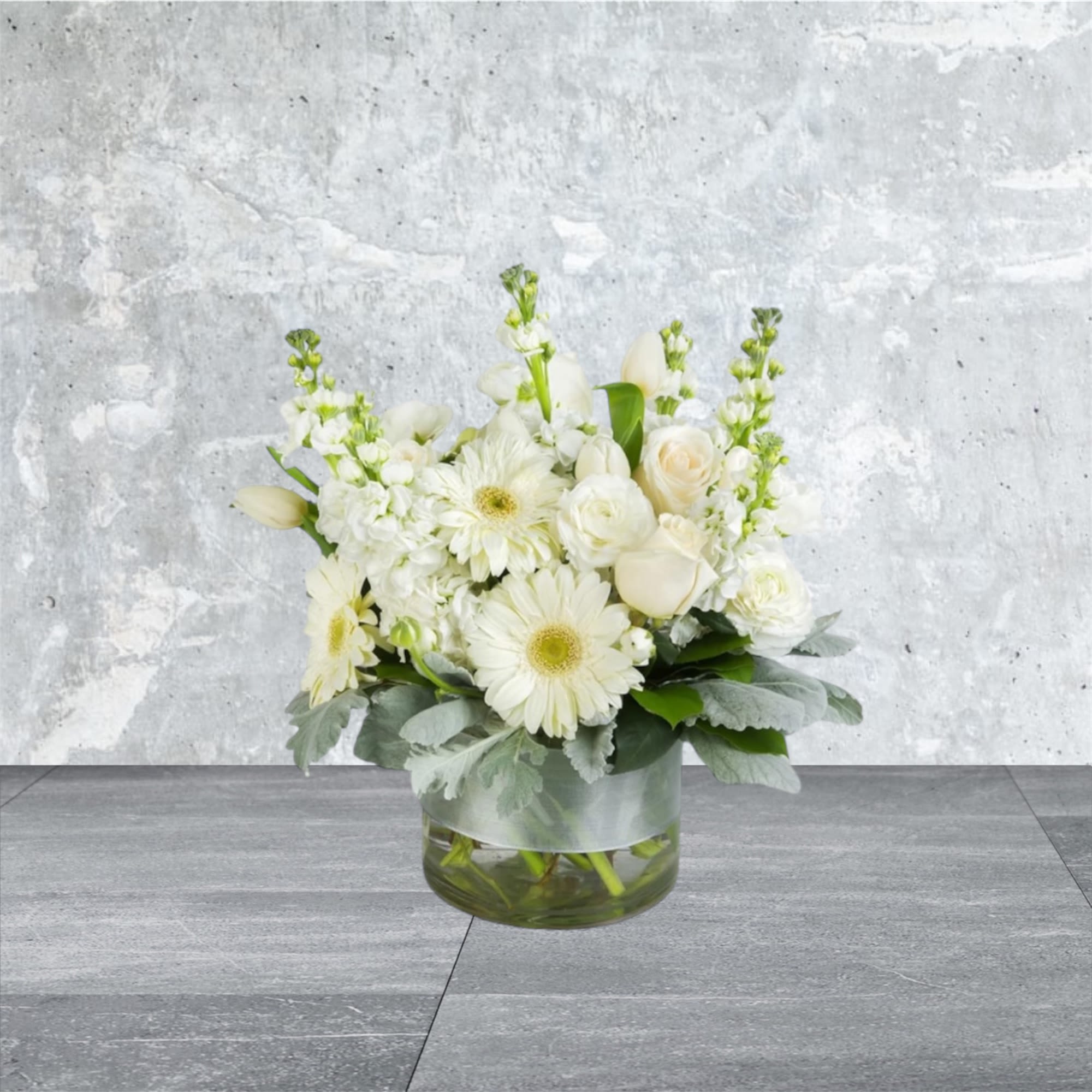 Purity - This arrangement contains gerbera daisies, roses, tulips, stock, and other seasonal blooms. APPROXIMATE DIMENSIONS: 15&quot; D x 13&quot; H