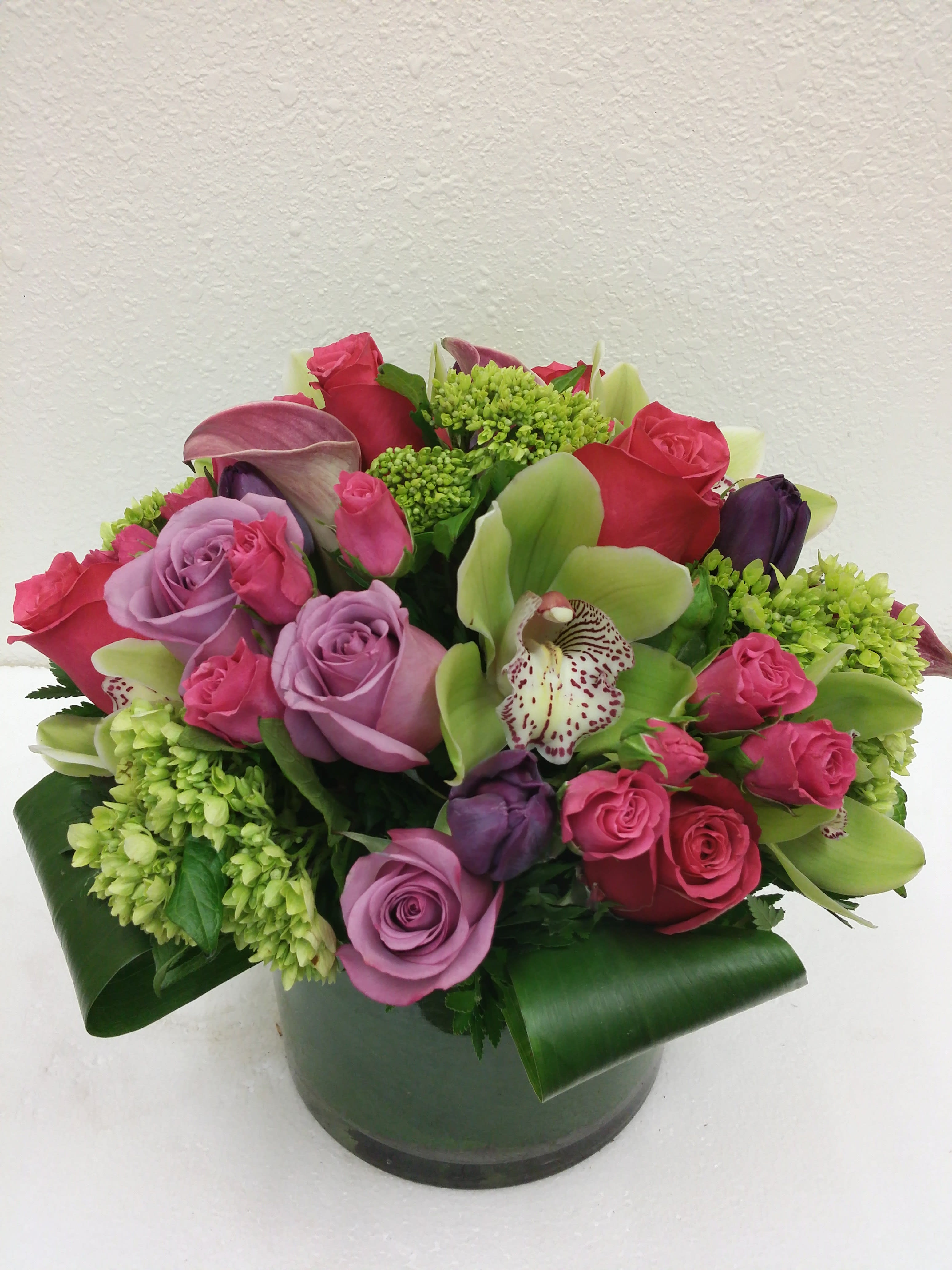 Floral Fantasia Floral Fantasia - Short modern contemporary styling in a cylinder vase, leaf lines with roses, spray roses, hydrangea and orchids, lush & full.