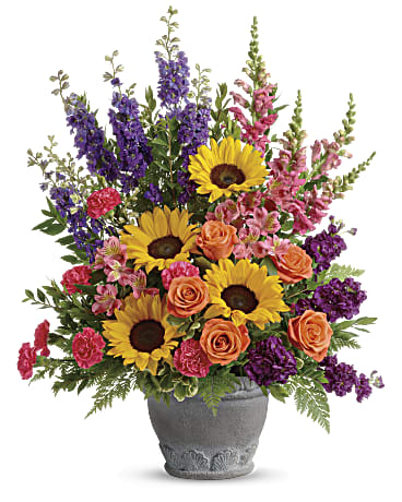 Hues of Hope Bouquet - Send a message of warmth and hope with this magnificent display of sunflowers and roses in a large antiqued pot, a colorful tribute that will warm their hearts. This bright arrangement includes orange roses, pink alstroemeria, hot pink carnations, yellow sunflowers, purple larkspur, purple stock, hot pink snapdragons, myrtle, variegated pittosporum, and leatherleaf fern.