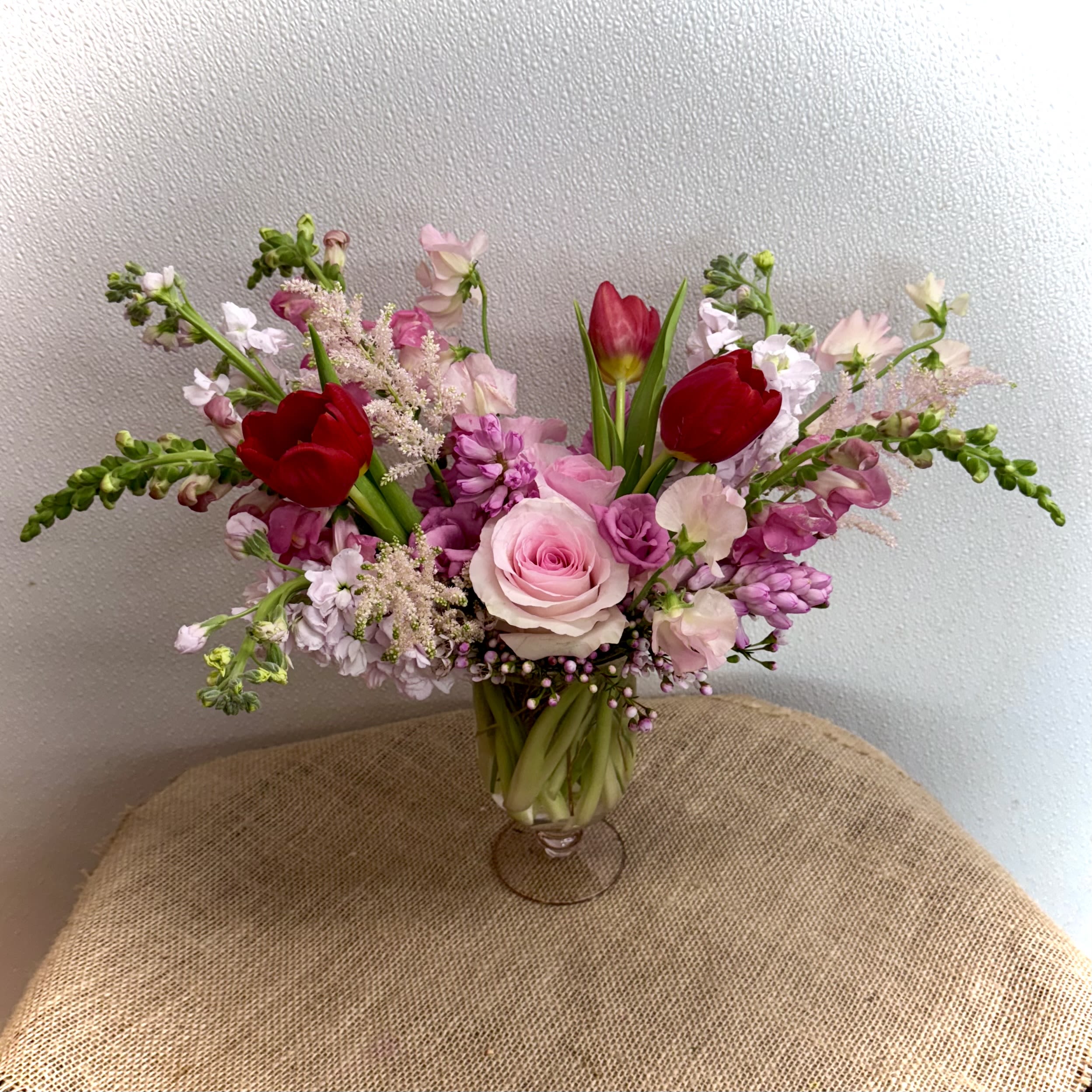 Baby, I'm Yours Baby, I'm Yours - Premium Assortment of Pink and Red Florals in a Pink Glass Pedestal Vase. Our Designers will arrange the mix of flowers based on availability and will maintain the general design of the photo.