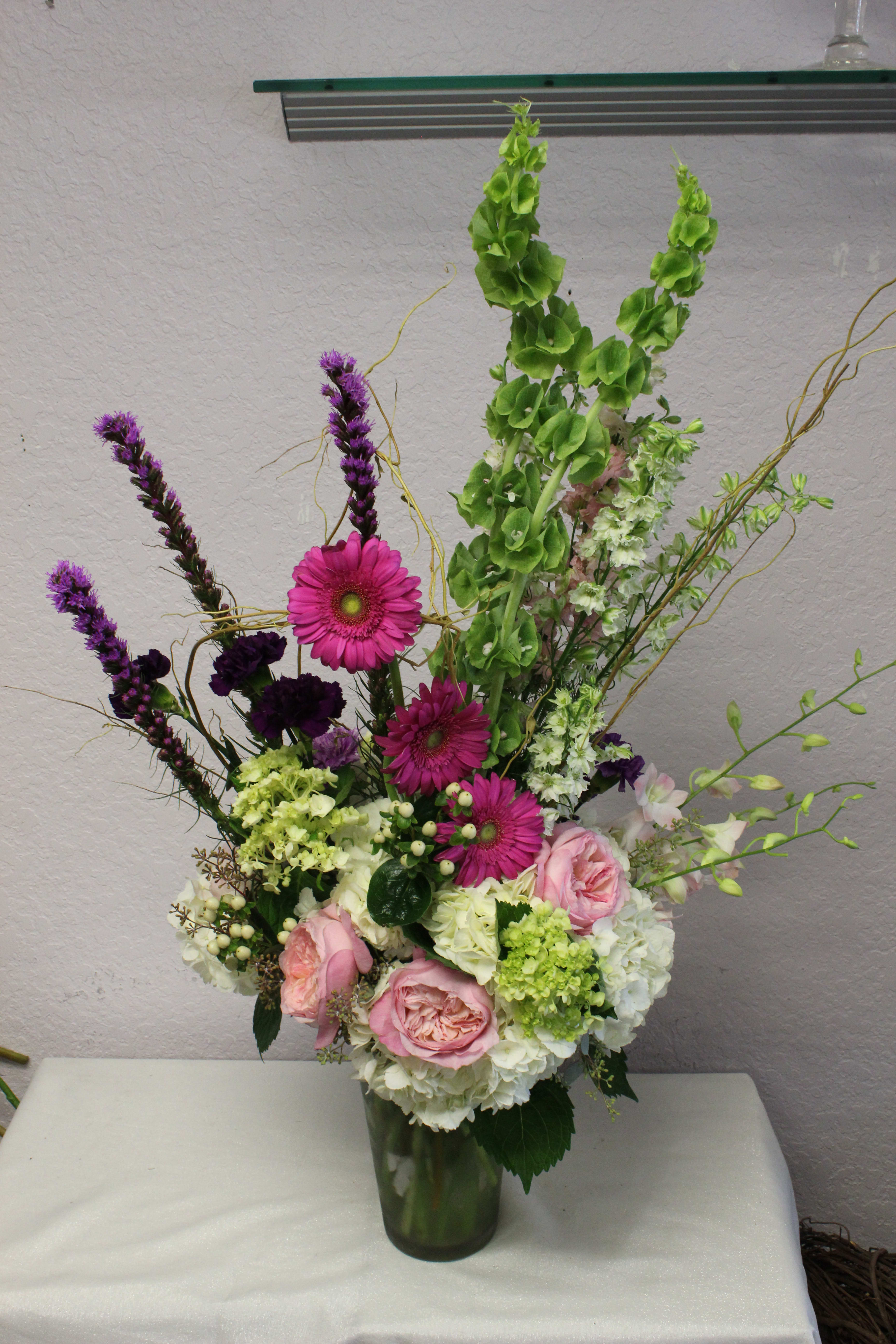 V109 - A high end grand, tall and showy arrangement consisting of beautiful flowers such as hydrangeas, roses, gerber daises, garden roses, larkspur, bells of ireland in pink, white and purple color tones. 