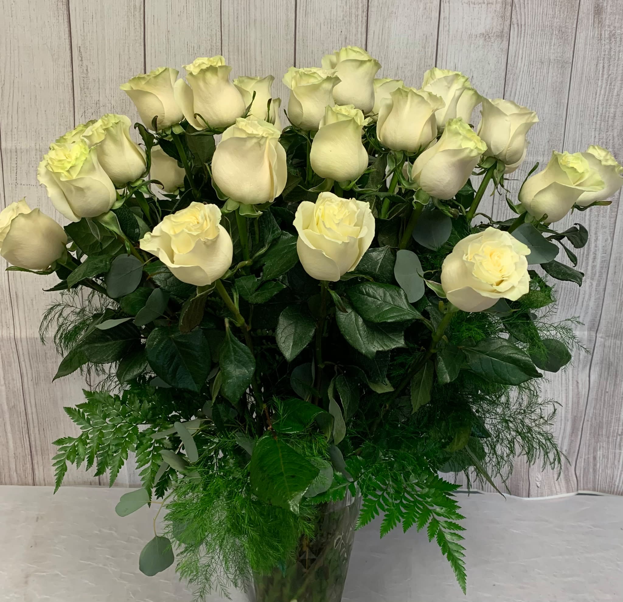 V116 - Two dozen white roses arranged in glass vase with mixed greenery. 