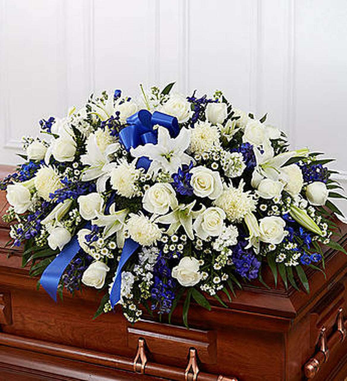 Cherished Memories Cherished Memories - Blue and white half casket spray Spray contains white roses, lilies, wax flower, mums, blue delphinium and palm leaves