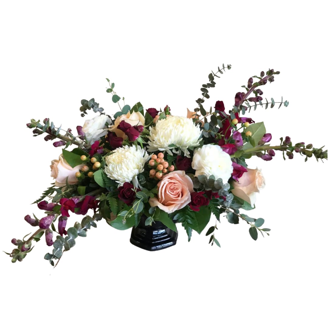 Love Spell Love Spell - Peach roses and hypericum, Burgundy snapdragons and spray roses, white football mums and ranunculus, speciality greenery in a black abby compote
