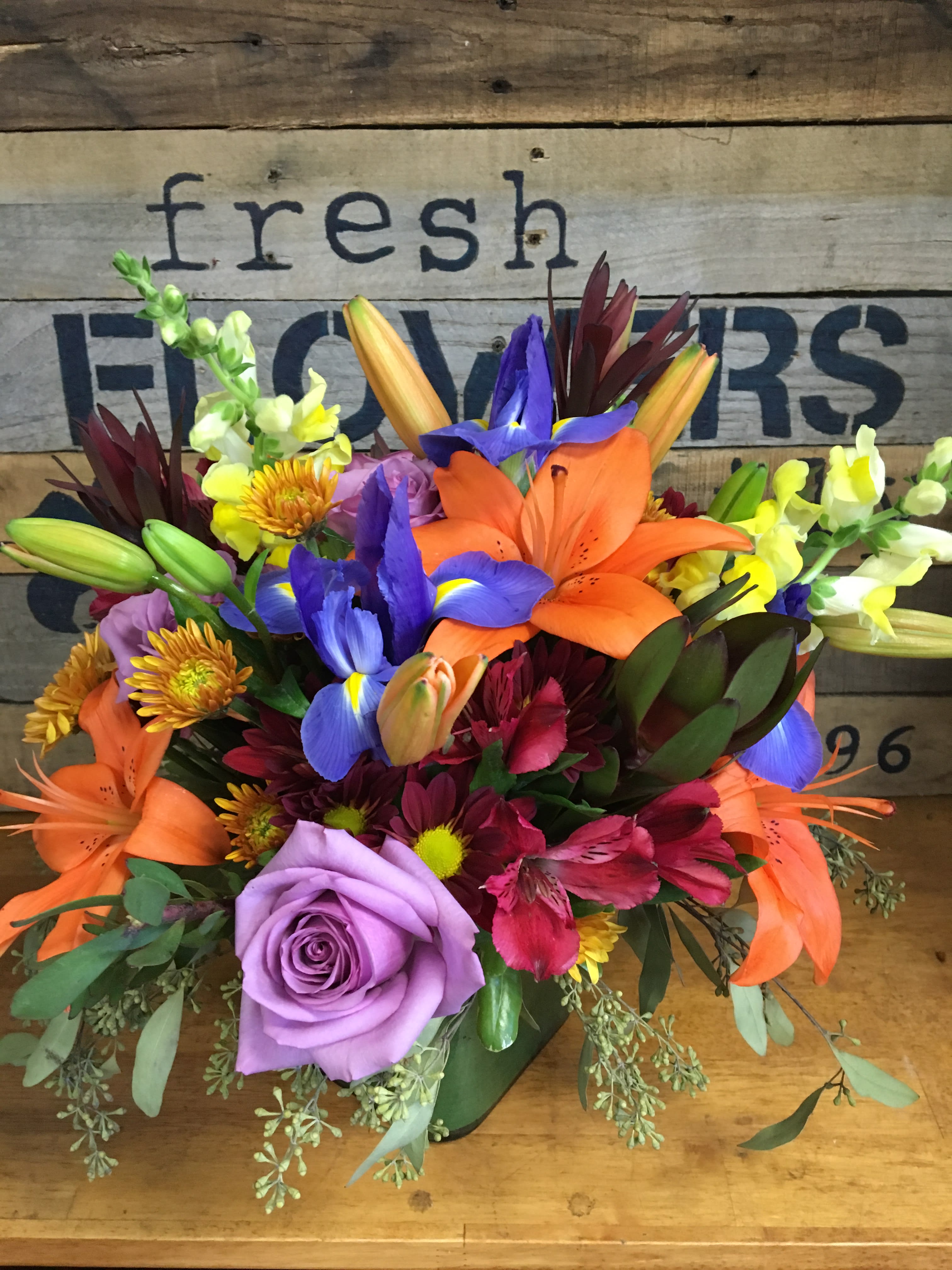 Flower Fusion Flower Fusion - Standard size is approx. 15"h x 14"w (pictured) A combination of bright bold colors come together in this exquisite arrangement with an autumnal feel. Arranged compactly in a glass cube lined with a leaf wrap.