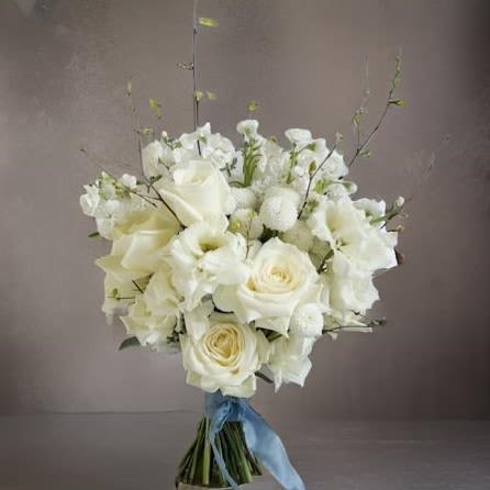 Timeless Ivory Bridal Bouquet with blue ribbon - The Timeless Ivory Bridal Bouquet is a stunning choice for brides seeking elegance and sophistication on their wedding day. Featuring luxurious white roses, lisianthus, and delicate accents of white craspedia, this bouquet exudes a soft yet classic charm. The bouquet is beautifully tied with a romantic blue silk ribbon, adding a subtle 'something blue' touch. Perfect for luxury weddings, this elegant white bouquet complements any bridal style, from modern to classic. Make a memorable statement with this exquisite wedding bouquet, crafted to enhance your walk down the aisle.