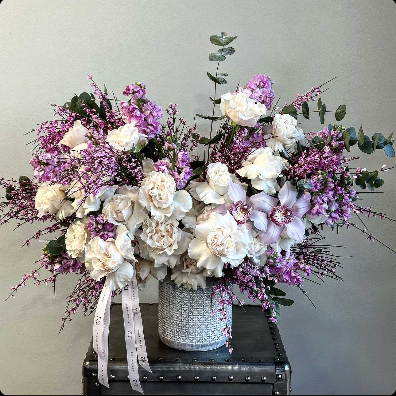 Alice Alice - Immerse yourself in the serene elegance of our vase arrangement, adorned with the exquisite beauty of roses, ethereal orchids, and aromatic eucalyptus. Each bloom and leaf is meticulously selected and delicately arranged to create a harmonious composition that captivates the senses. The soft petals of roses complement the delicate allure of orchids, while the refreshing scent of eucalyptus adds a touch of tranquility to the ensemble.