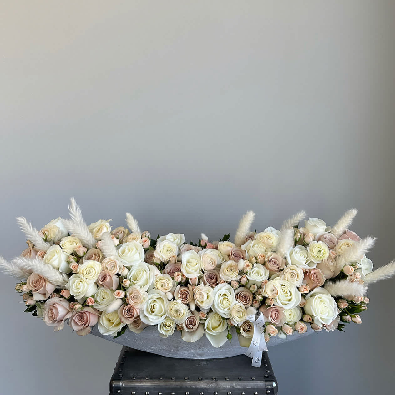 Furiosa Furiosa - This exquisite arrangement features a stunning combination of nude flowers in a chic stone vase. The arrangement includes a mix of roses, spray roses, and ranunculus, all in delicate shades of nude that creates a soft and romantic look.
