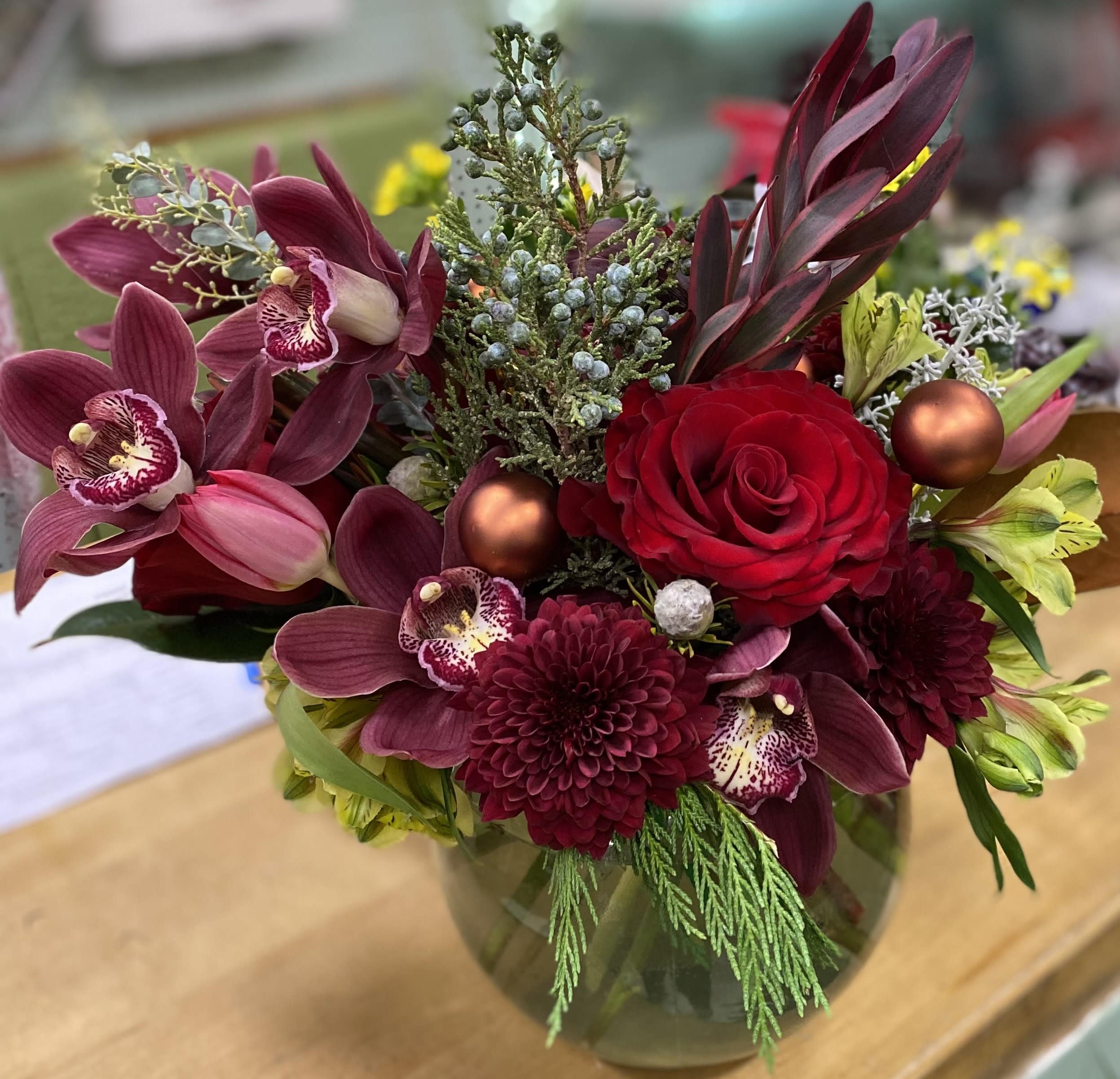 Burgundy Christmas - This vase arrangement is made with deep red roses, orchid, and cremon in a round bubble bowl, this makes the perfect charismas arrangement or for a special anniversary.