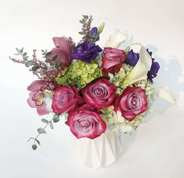 Gerald  - This brightly colored pink and purple vase arrangement is accentuated with a unique twist by adding burgundy orchids. Each color becomes even brighter with the help of white calla lilies and green hydrangea. This arrangement is presented in a clear pinched glass vase.   Flowers and vase may vary based on availability.