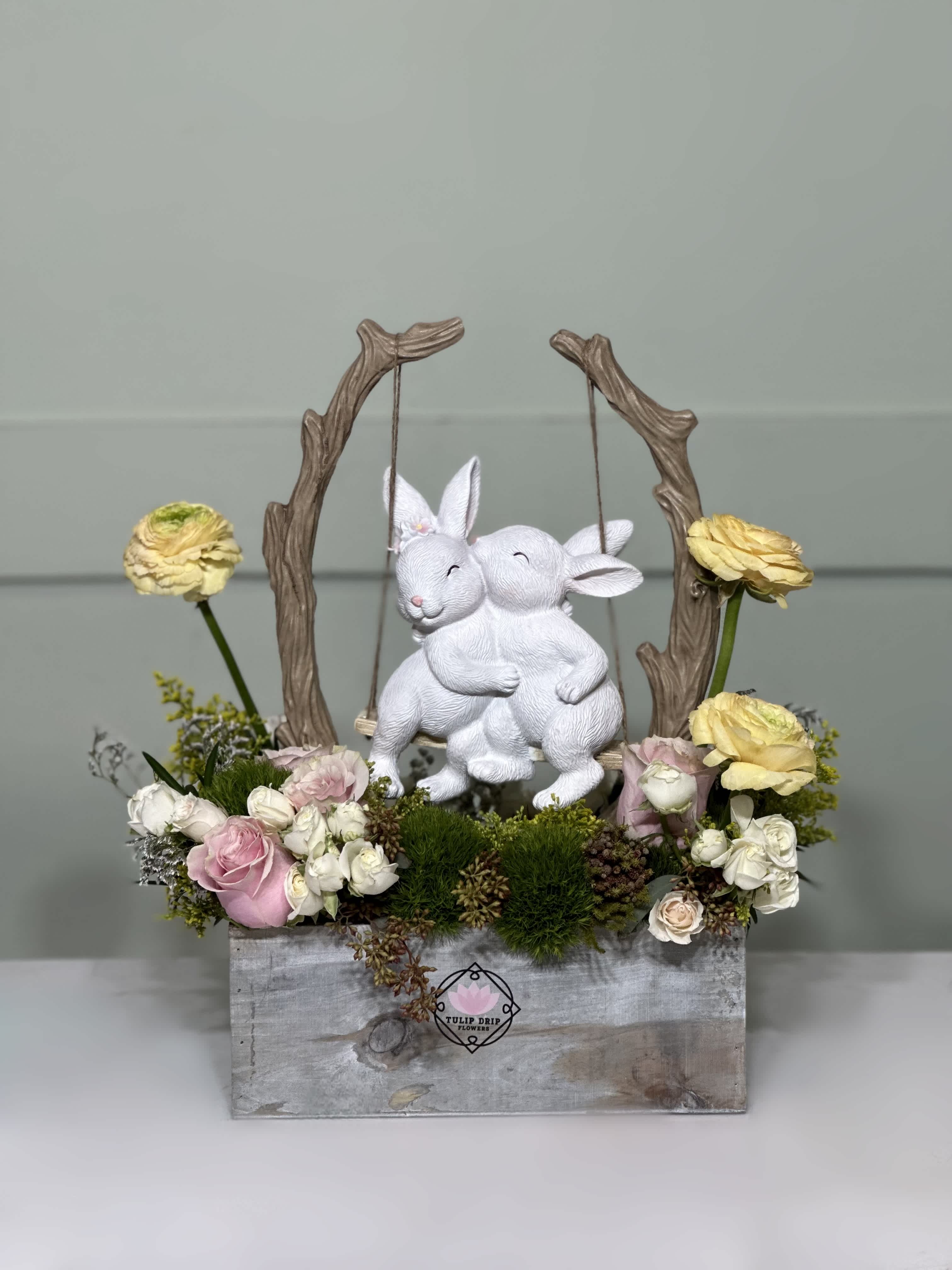 Bunny Love  - Roses, Ranunculuses , Spray roses and a ceramic statue of two loving bunnies in a wooden box .  