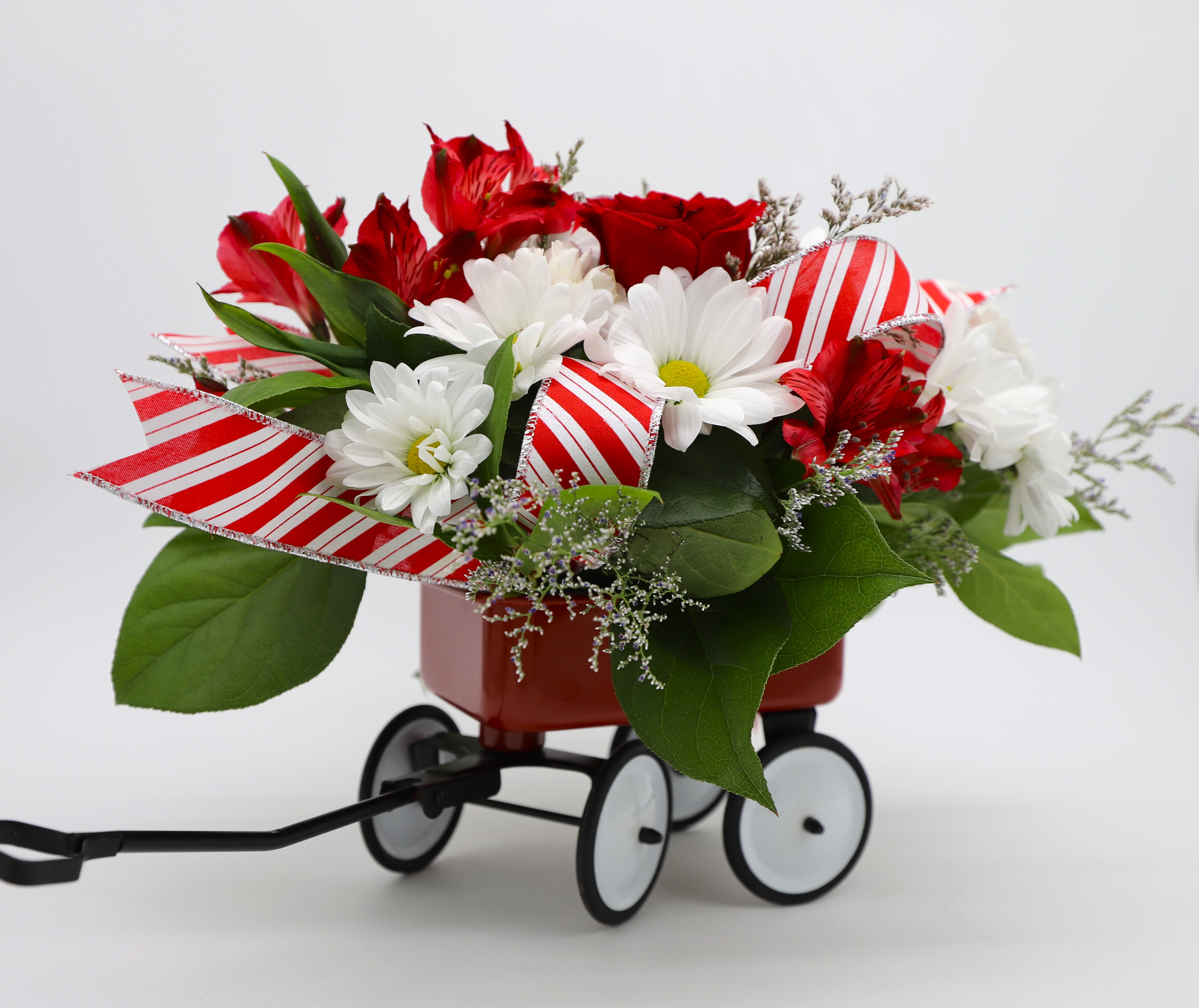 Wonderland Wagon - Send your loved ones holiday cheer in a jolly red wagon! This beautiful arrangement includes roses, alstromerias, daisies, greenery and filler flowers in a red functional wagon.