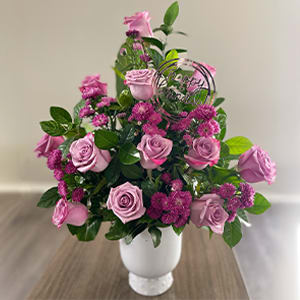 Garden Dreams - Delightful floral arrangement of long stem purple roses, purple asters and assorted greenery on a white vase.
