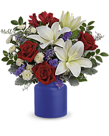 Rose Revelry - White asiatic lilies, red roses, red alstroemeria, white button spray chrysanthemums, purple sinuata statice and misty blue limonium are accented with dusty miller and huckleberry. Delivered in  Savannah Jar.