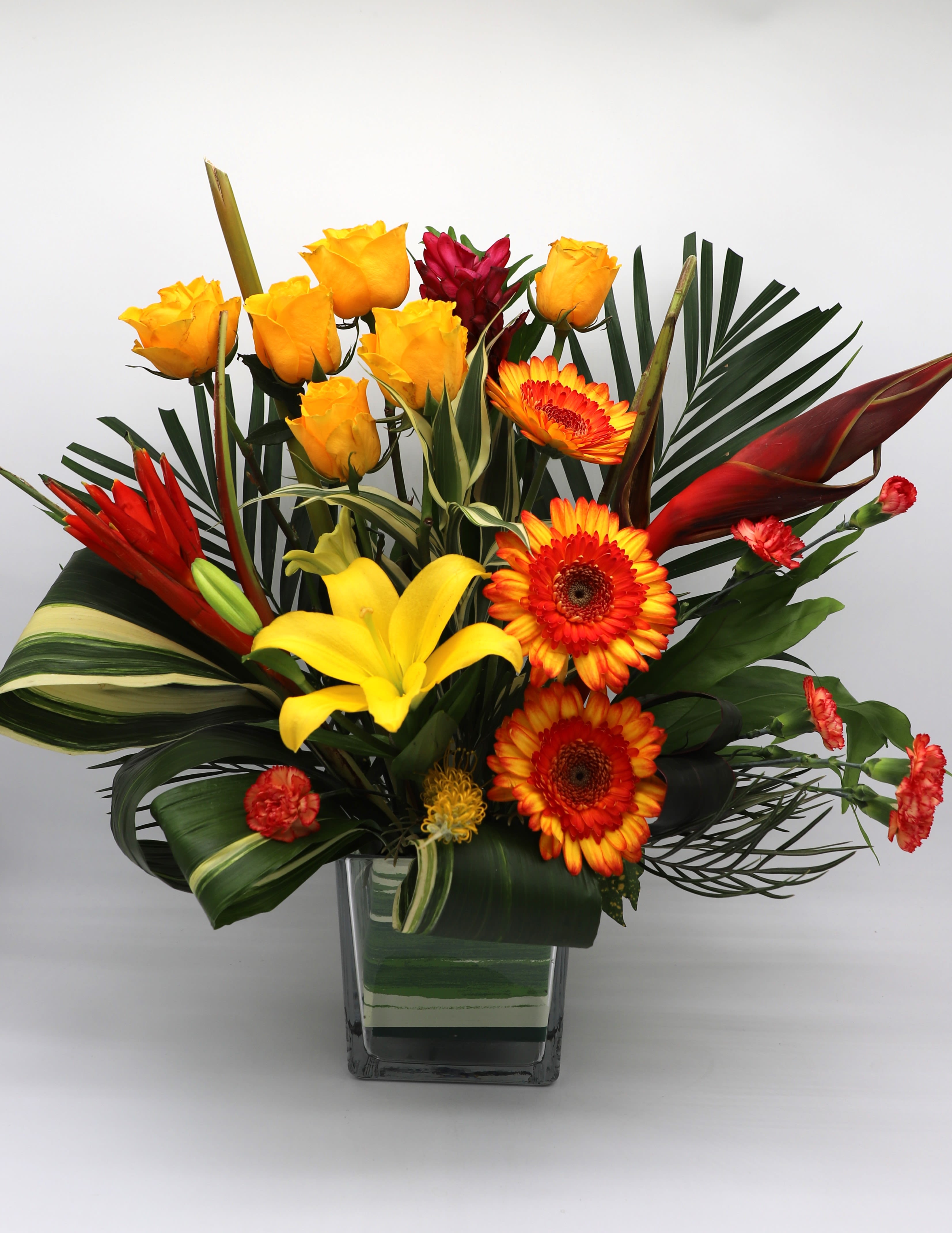 Aloha Sunrise - This vase arrangement includes yellow roses, bicolor gerber daisies, bicolor mini carnations, and yellow lillies with stunning tropical flowers and greenery.