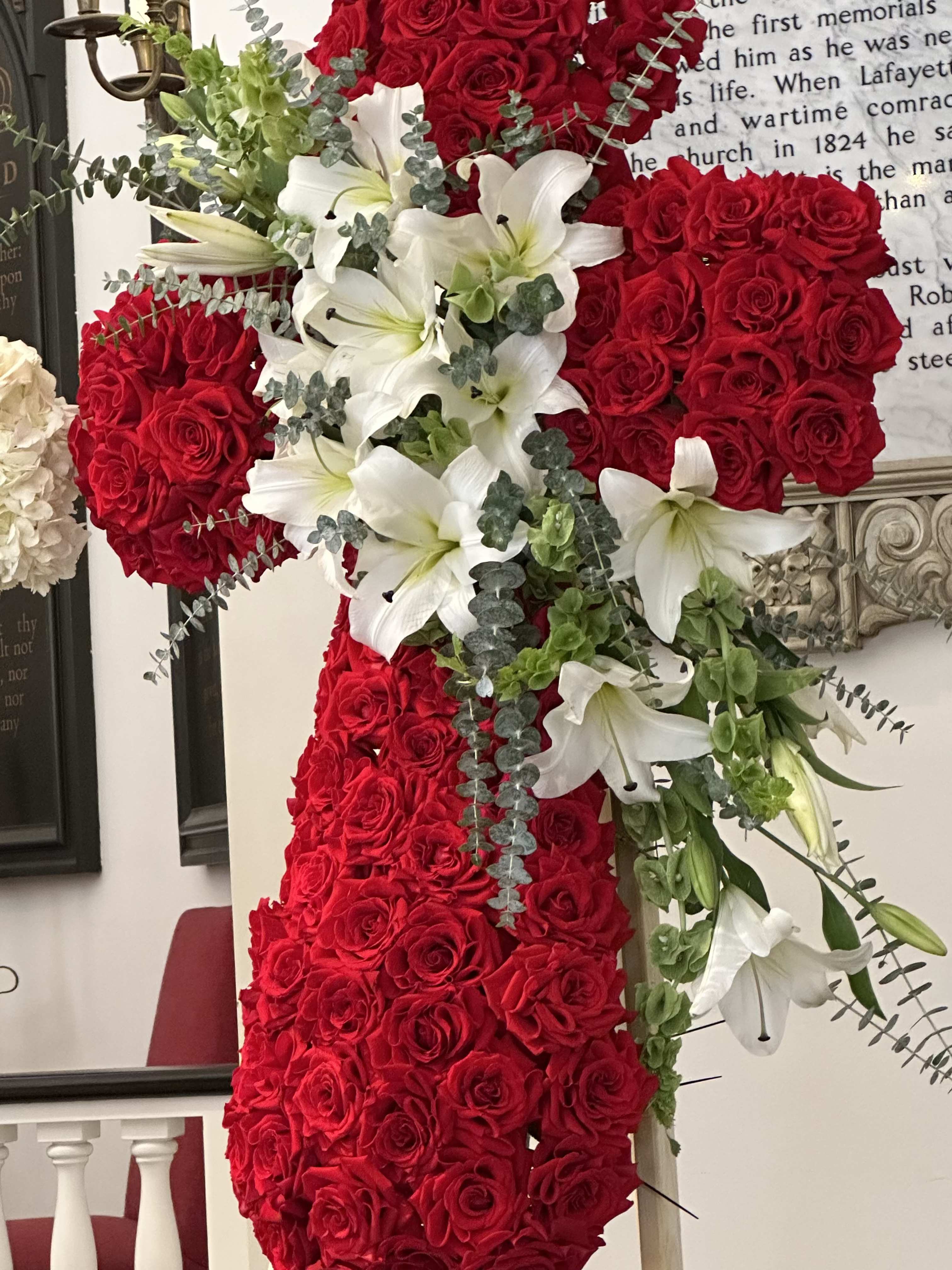 Red Rose Cross By VLM Flowers - The Red Rose Cross is a very elegant funeral cross with a ribbon made out of Lilies and Bells. The picture is not the standard price. The picture is the deluxe price.
