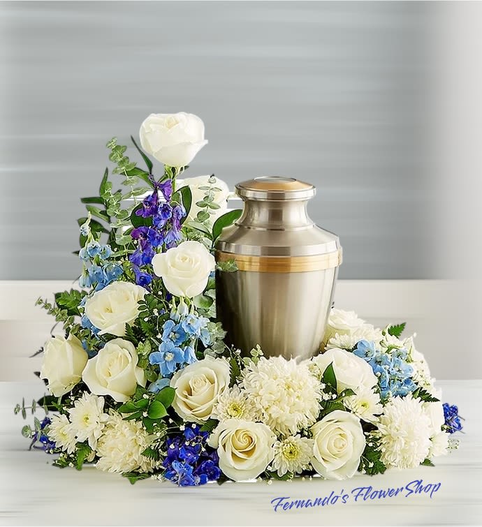 Whispered Prayers - This graceful cremation floral arrangement is a dignified and heartfelt tribute. Designed to frame and honor an urn, it features a beautiful combination of white roses, chrysanthemums, and delphiniums, accented with soft blue flowers and eucalyptus greenery. The white flowers symbolize peace and purity, while the blue tones add a serene and calming touch. The arrangement’s thoughtful design exudes elegance and reverence, providing comfort and a sense of tranquility during a time of remembrance. A fitting way to celebrate a cherished life with love and dignity.
