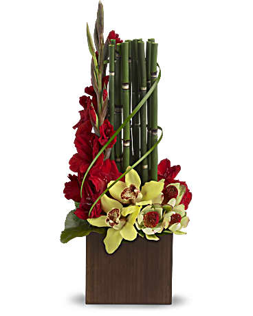 Fantasy Found Fantasy Found - Yellow cymbidium orchids, red gladioli and yellow leucadendron are presented in a dark bamboo vase with lily grass, bamboo-like equisetum and galax leaves.